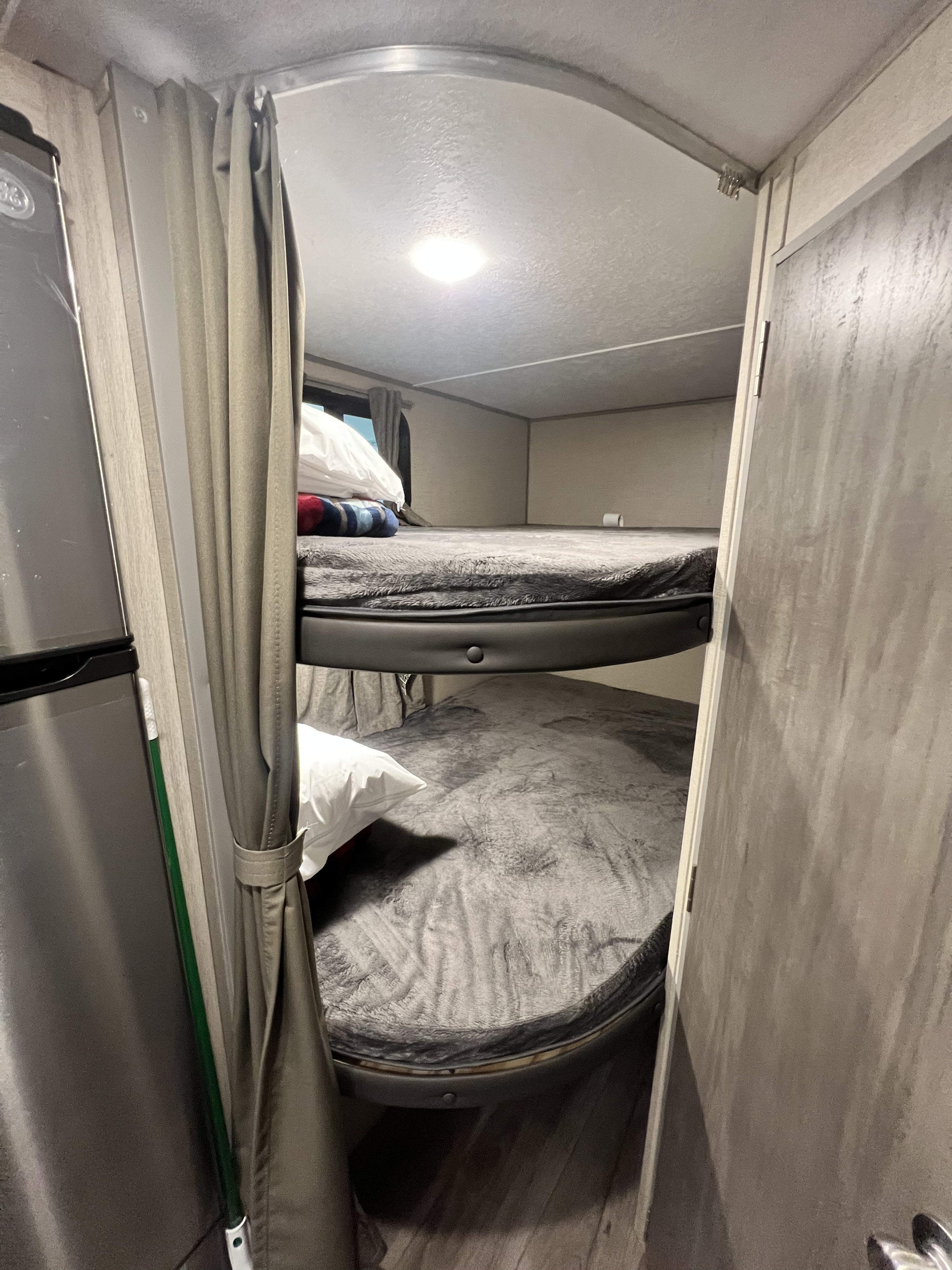 Compact RV rental sleeping area: two stacked bunk beds with grey bedding, privacy curtains, and a fridge nearby.. Forest River Coachmen Catalina Summit 2022