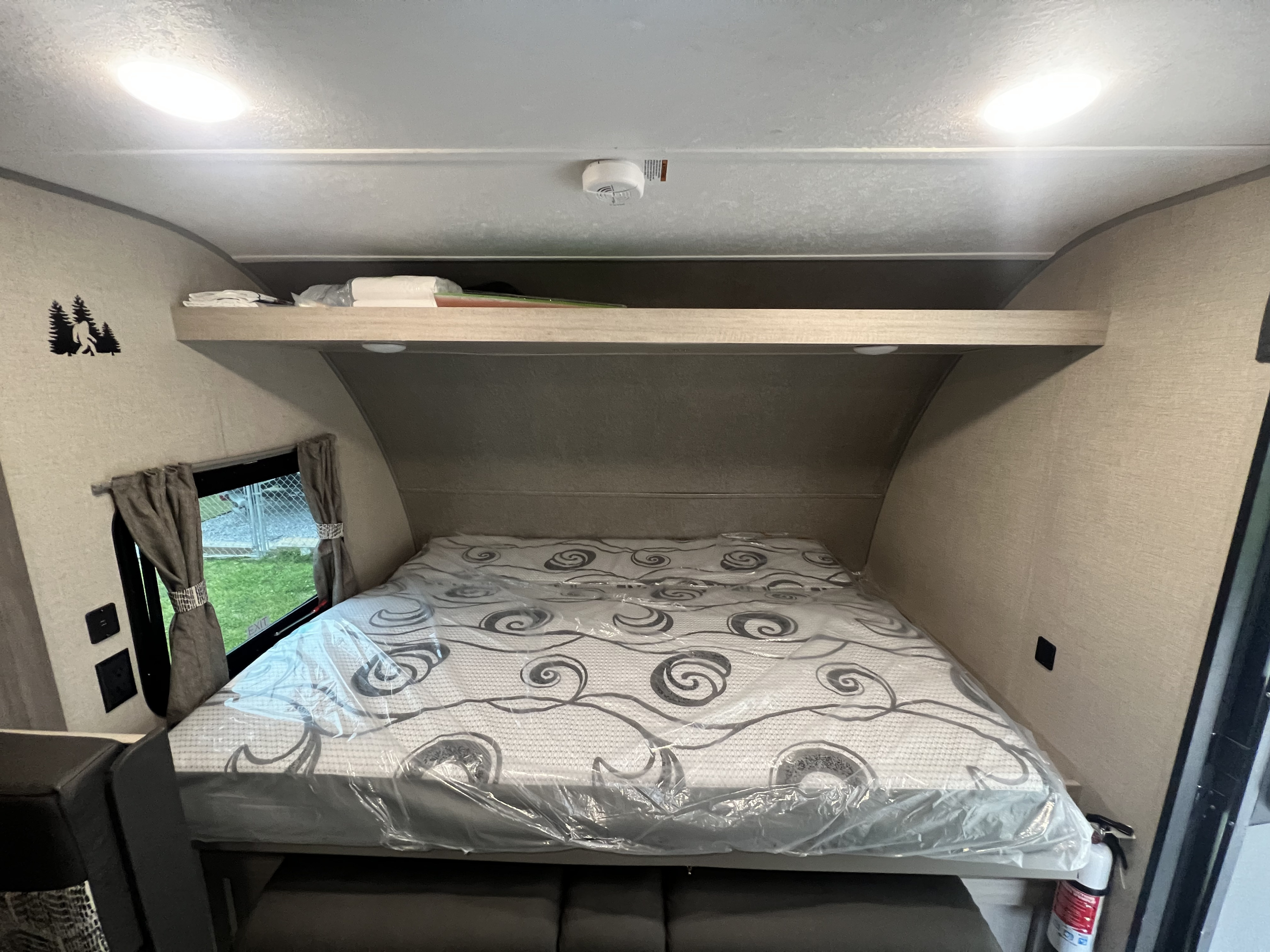 This RV rental interior features a cozy bed with mattress cover, overhead shelf, window, and essential safety items.. Forest River Coachmen Catalina Summit 2022