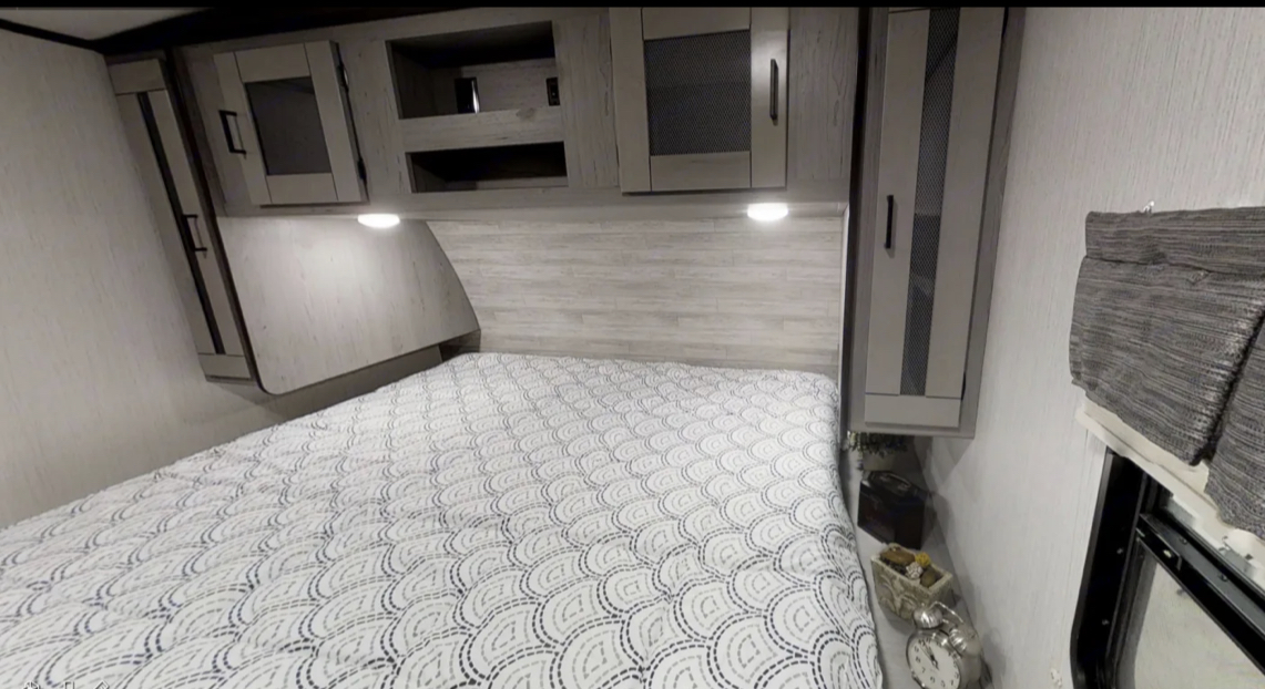 Inside an RV rental, a cozy bedroom boasts a patterned bed, storage cabinets, and ambient lighting above the headboard.. Heartland RVs Mallard 2021