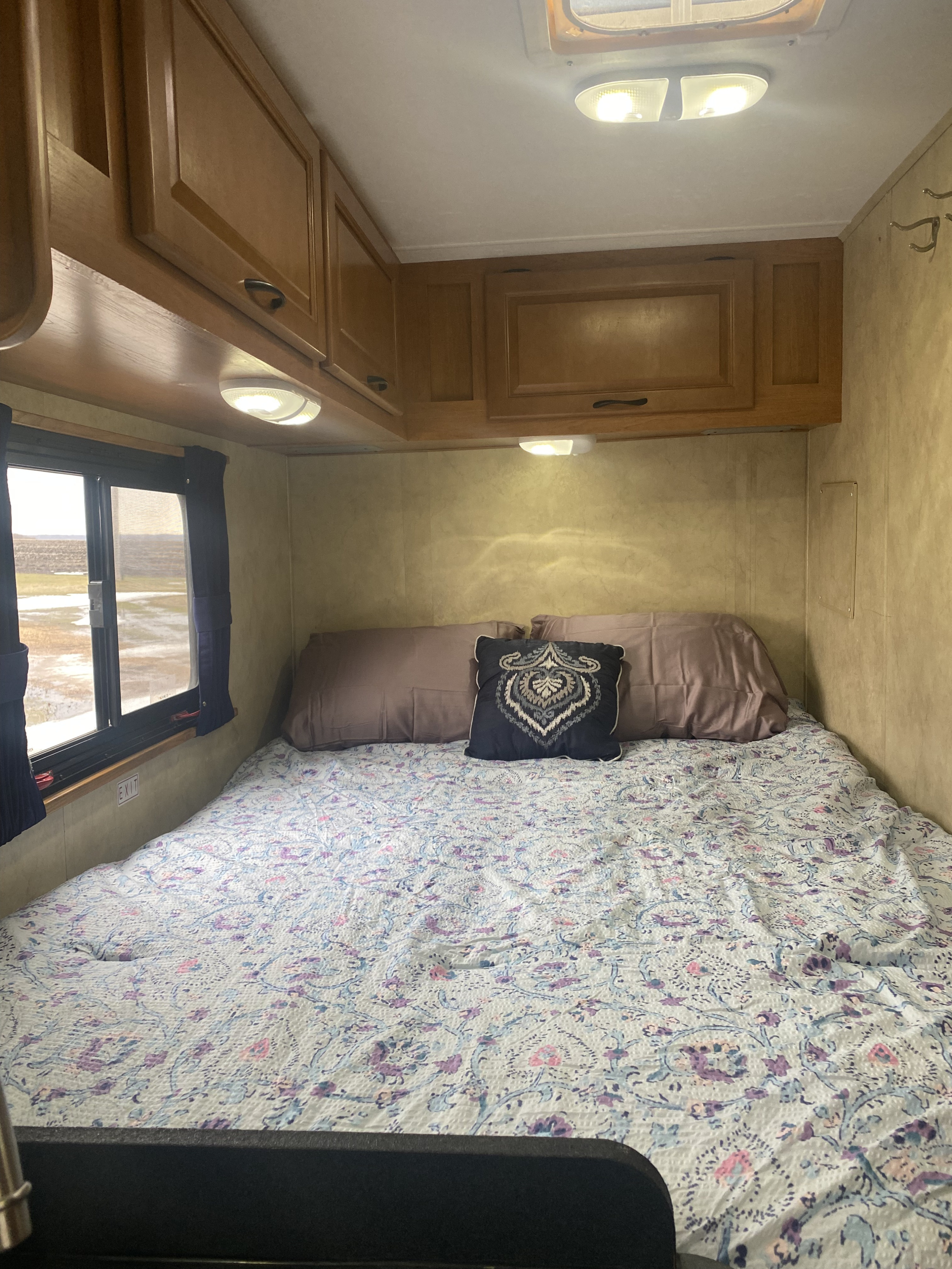 Cozy RV rental bedroom featuring a patterned bedspread, wooden cabinets, and a window view with an "EXIT" sign.. Thor Majestic 2013