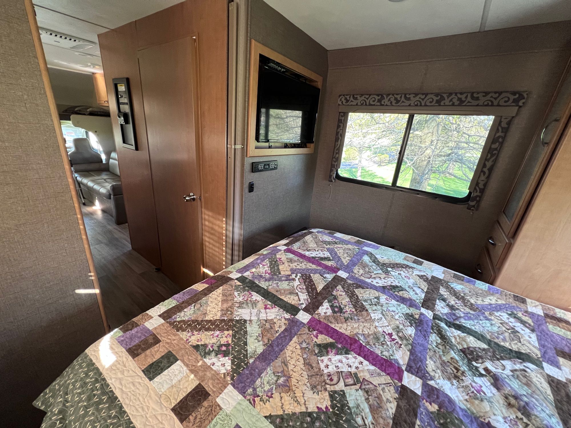 Cozy RV rental bedroom with a colorful quilted bed, wall-mounted TV, and window showing outdoor scenery.. Thor Four Winds 2017