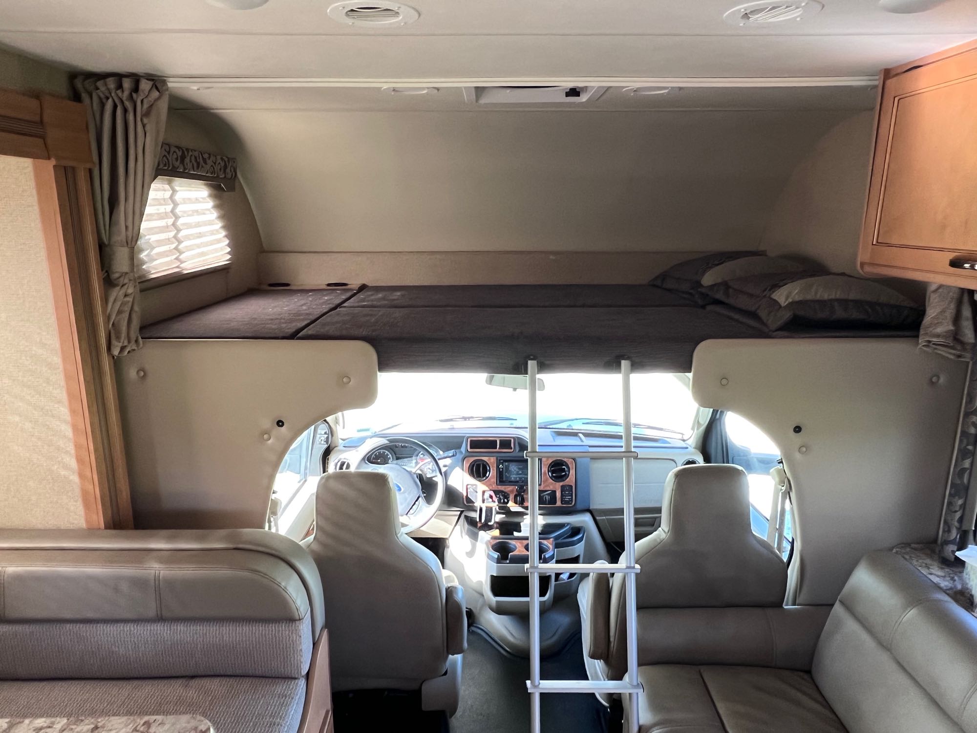 Spacious RV rental interior, showcasing the over-cab bunk bed with ladder, driver's cockpit, and comfortable seating.. Thor Four Winds 2017