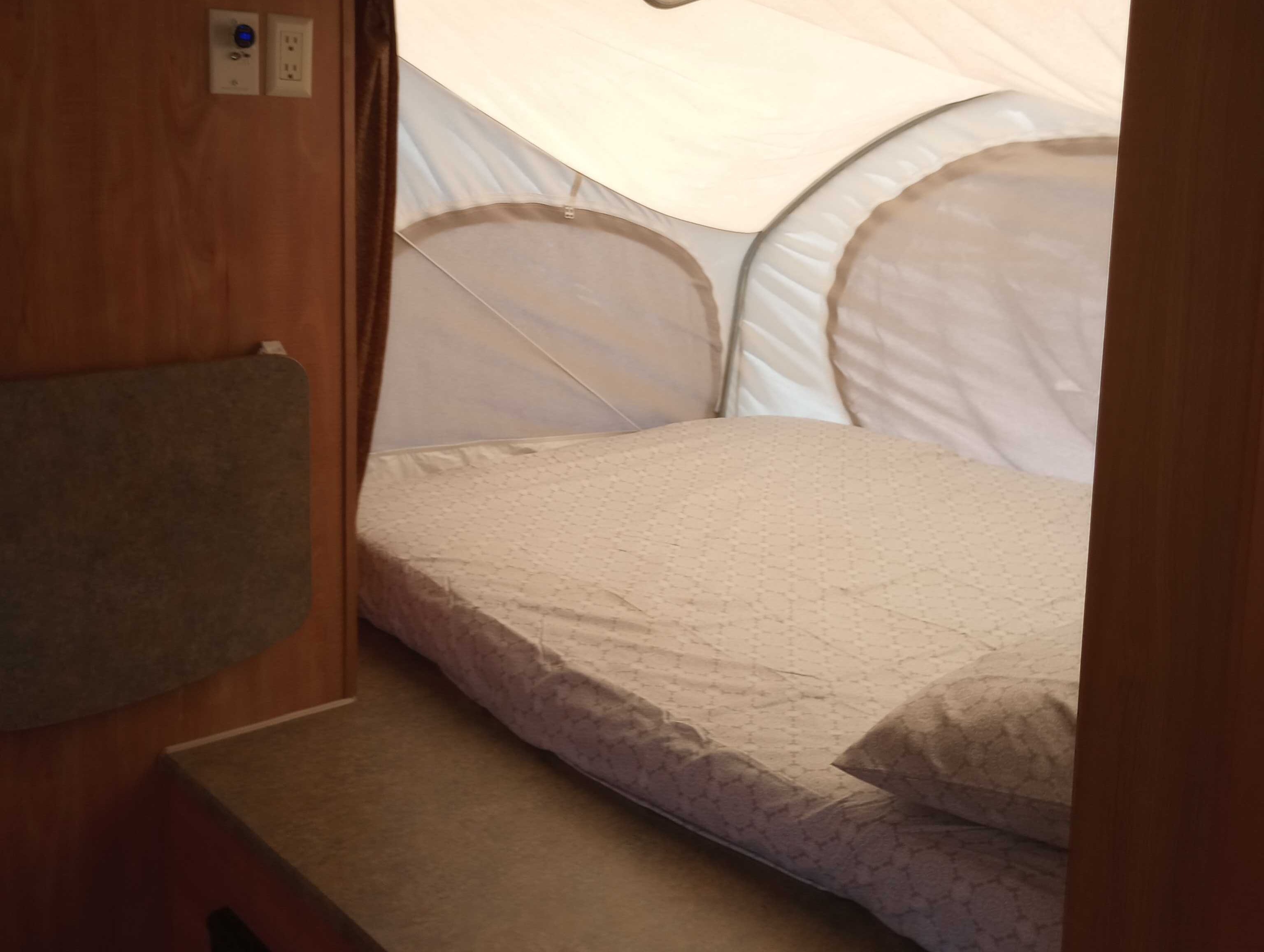 RV rental pop-up camper: Interior view of the bed with patterned sheets, pillow, and wall-mounted electrical outlets.. Thor Skamper Kodiak 2009