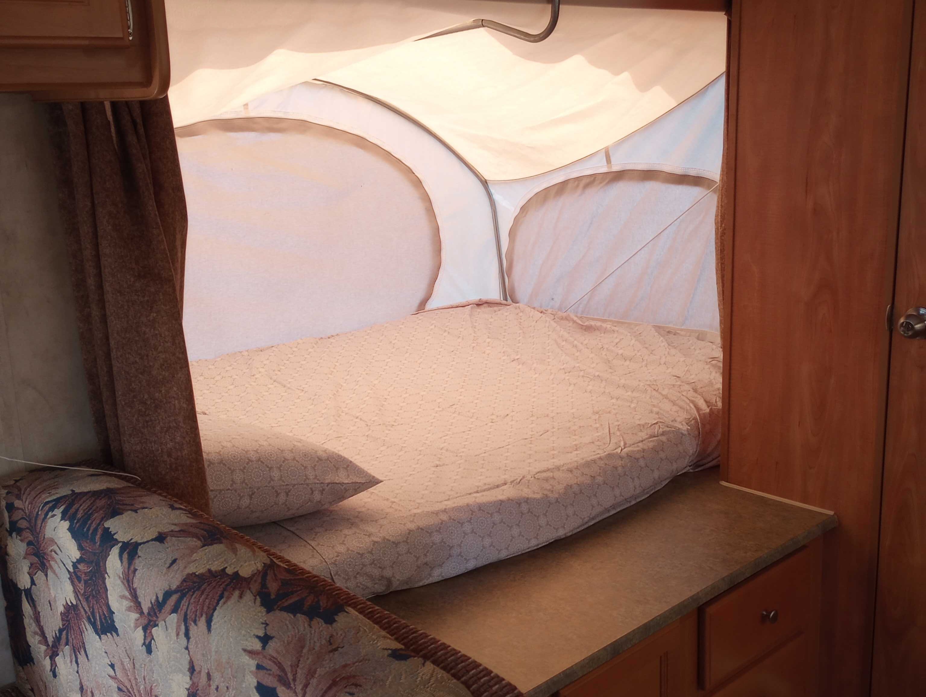RV rental interior: a comfy, quilted bed in the pop-out tent section, with wooden cabinetry and brown curtains.. Thor Skamper Kodiak 2009