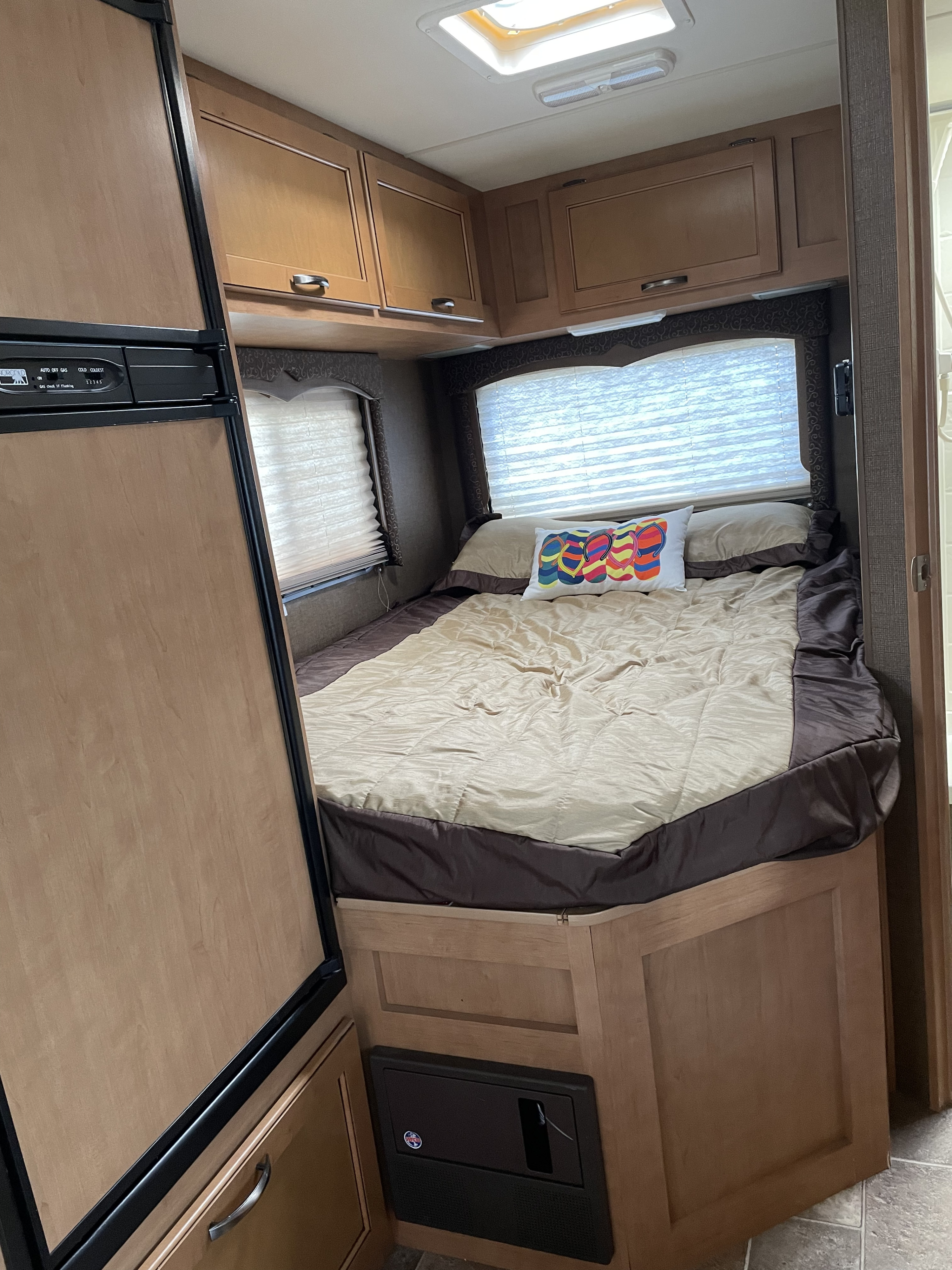 Cozy RV rental bedroom showing a comfortable bed, overhead cabinets, and a compact refrigerator on the left.. Thor Four Winds 2015
