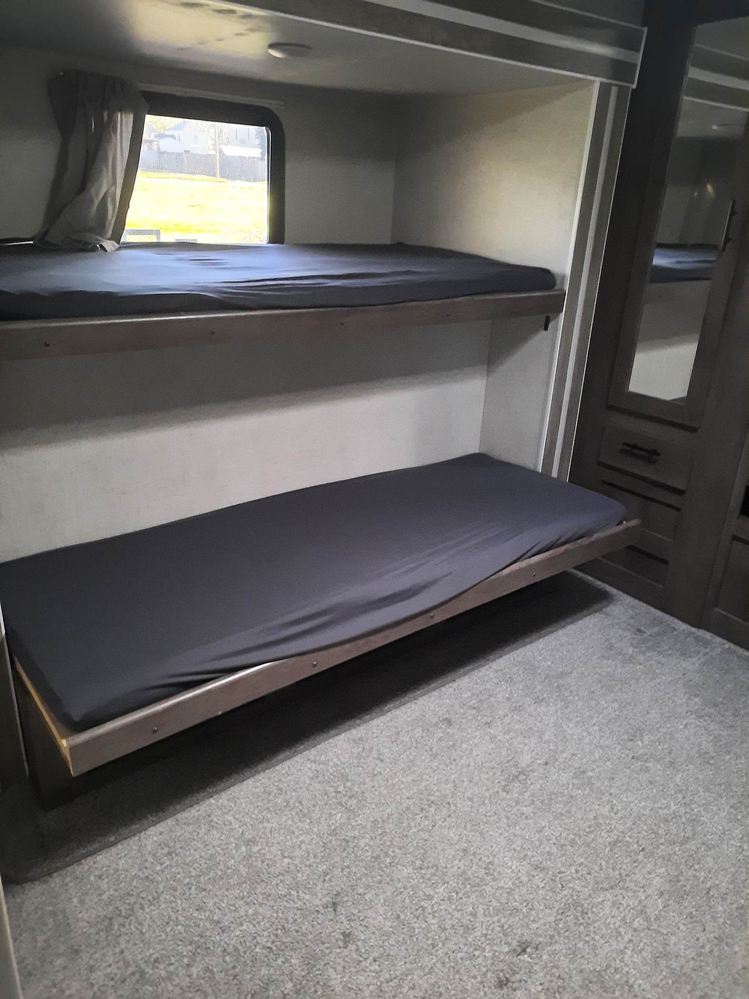 Explore this RV rental's cozy bunk beds with dark sheets. Top bunk offers a bright window view; lower bunk is floor level.. Forest River Wildwood 2021
