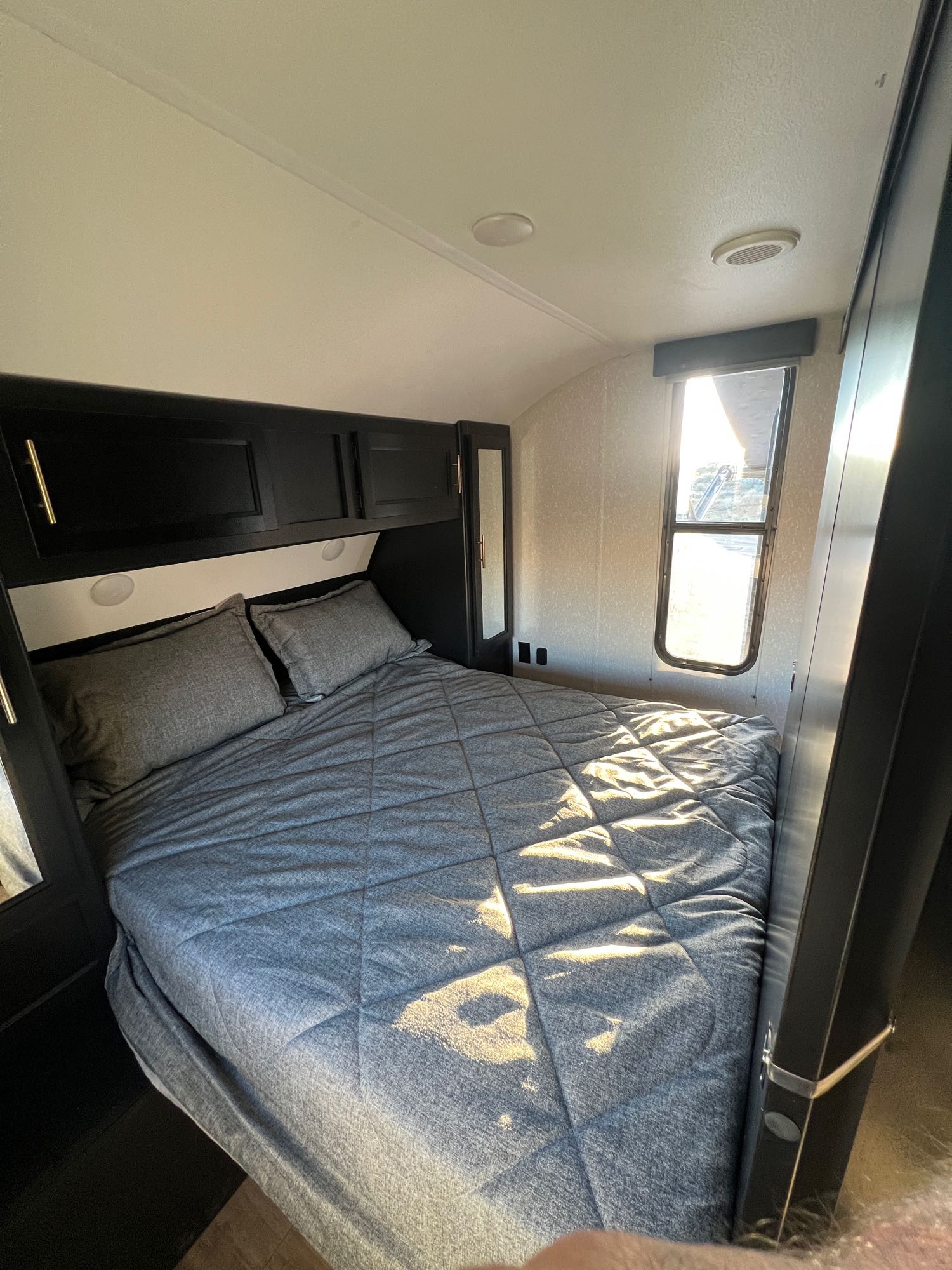 Comfortable RV rental bedroom with a bed, dark cabinets, and sunlit window. Your cozy sleeping area.. Forest River Cherokee Grey Wolf 2022