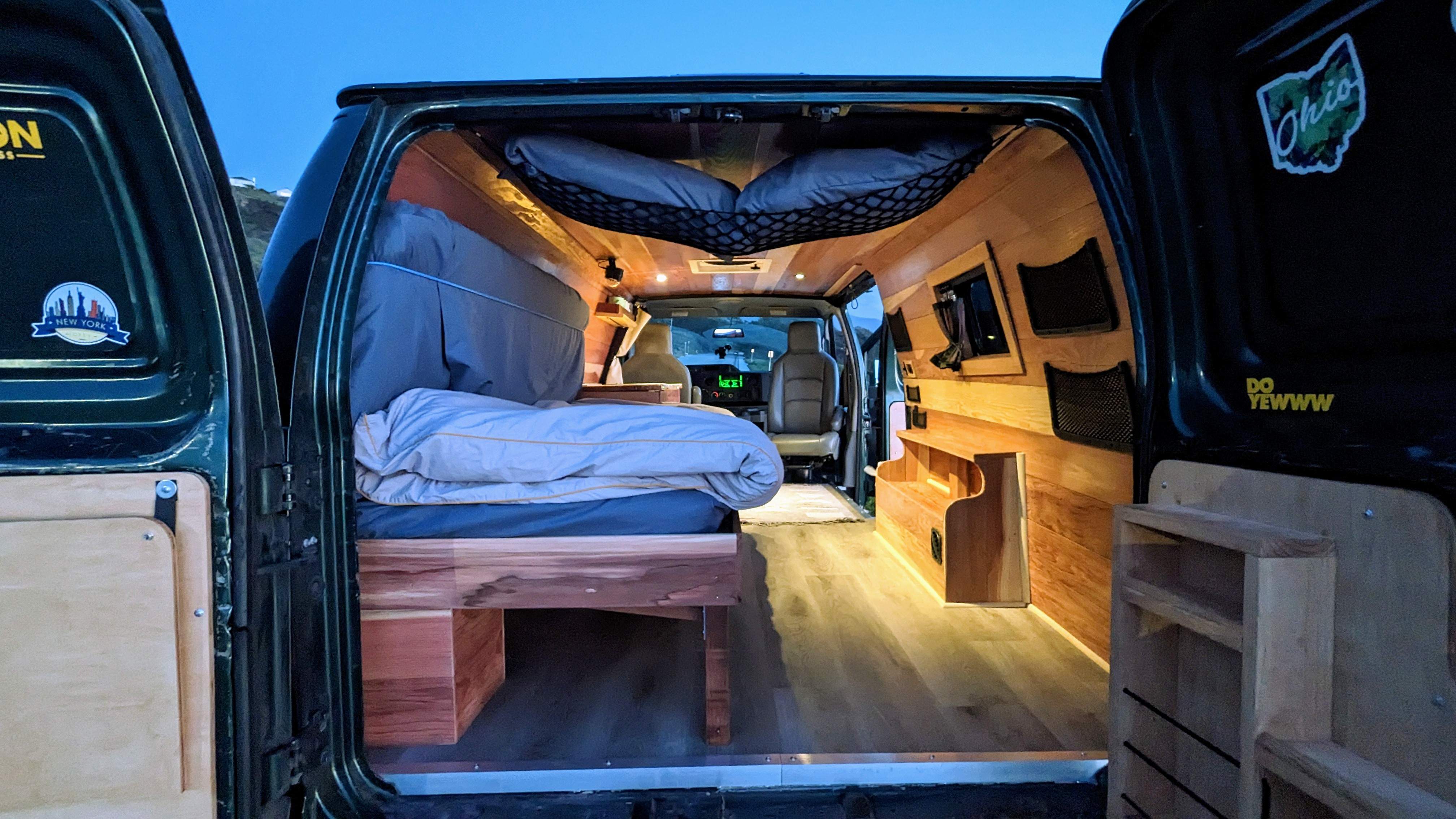Cozy RV rental campervan interior: custom wood paneling, bed, and smart storage for your mobile living adventures.. Ford Econoline 2009
