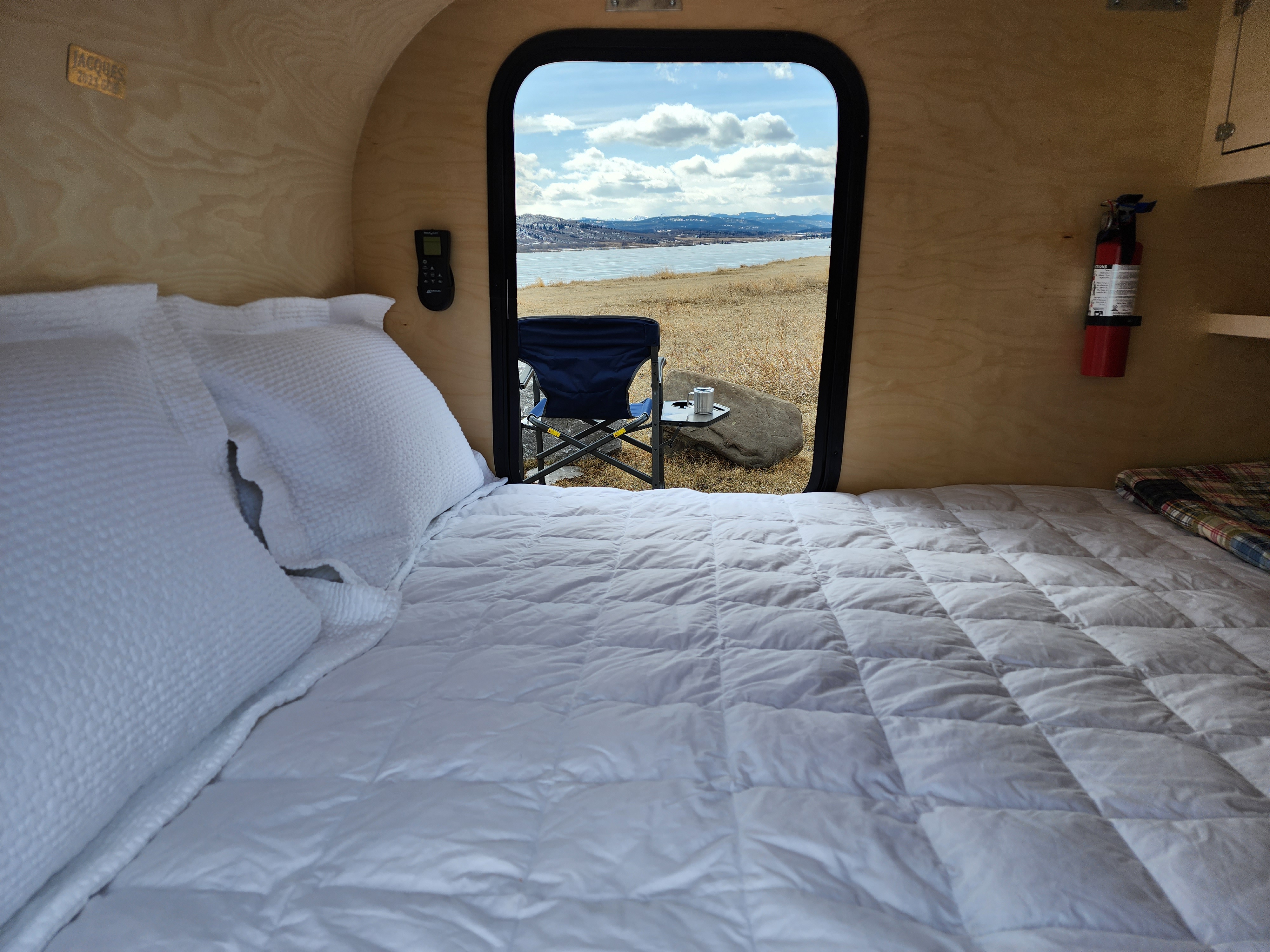 Inside a cozy RV rental, a bed with white bedding faces an open door with a beautiful lake and mountain view.. Gnome Home Gnome Home 2023