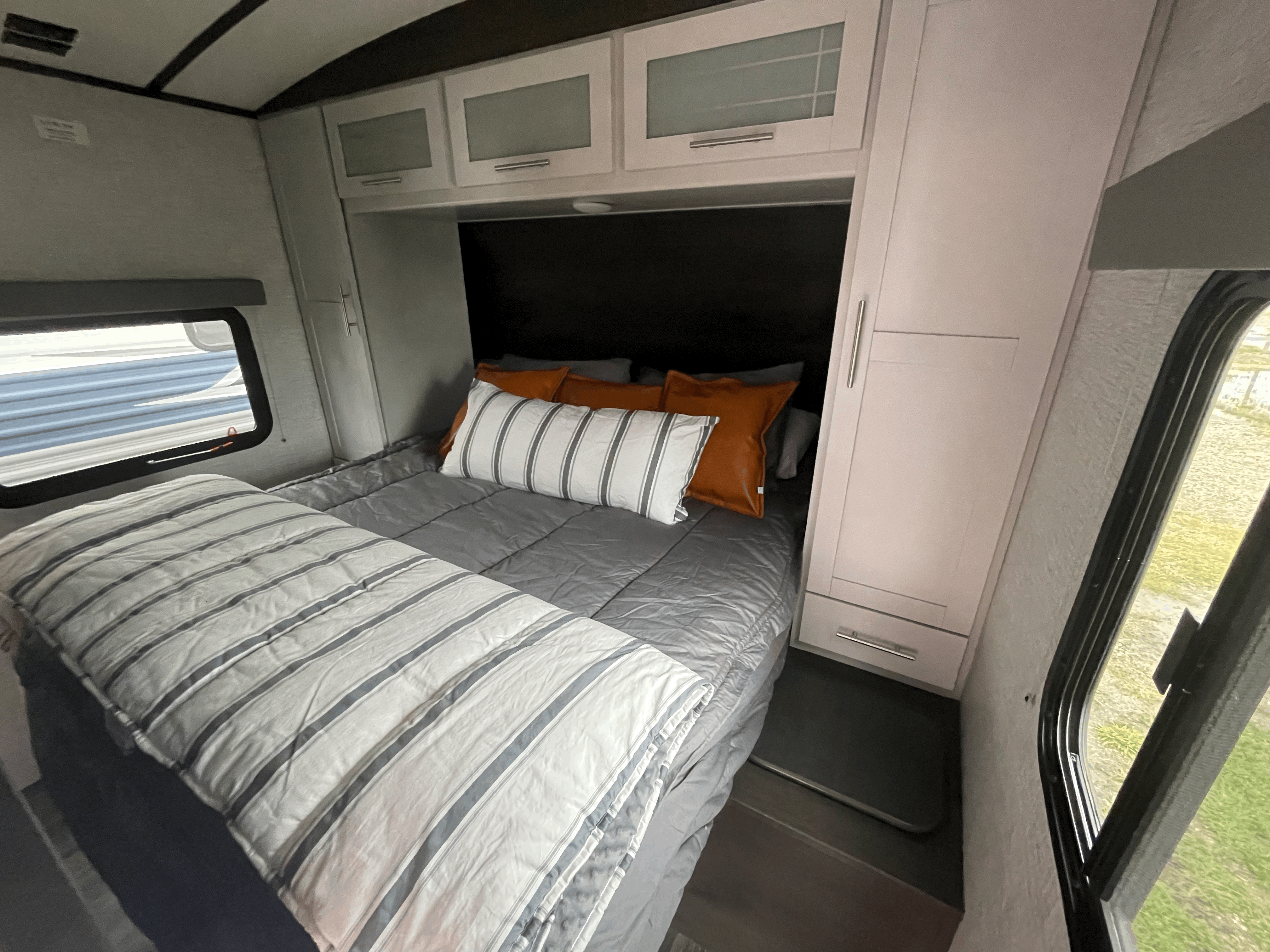 Cozy RV rental bedroom with striped bedding, orange accent pillows, light cabinetry, and a window, offering comfort on the go.. Keystone RV Bullet Ultra Lite 2021