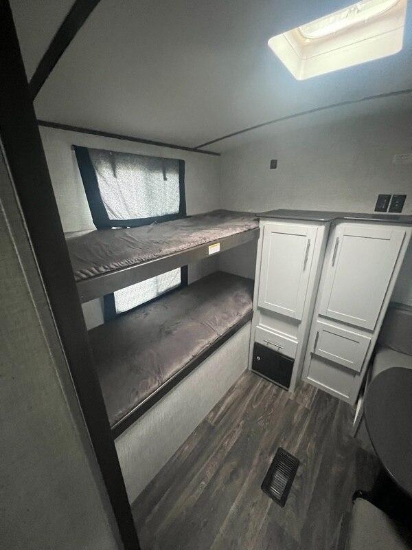 Inside an RV rental: two bunk beds with mattresses, storage units, and part of a dinette area. A skylight illuminates the space.. Keystone RV Bullet Ultra Lite 2021