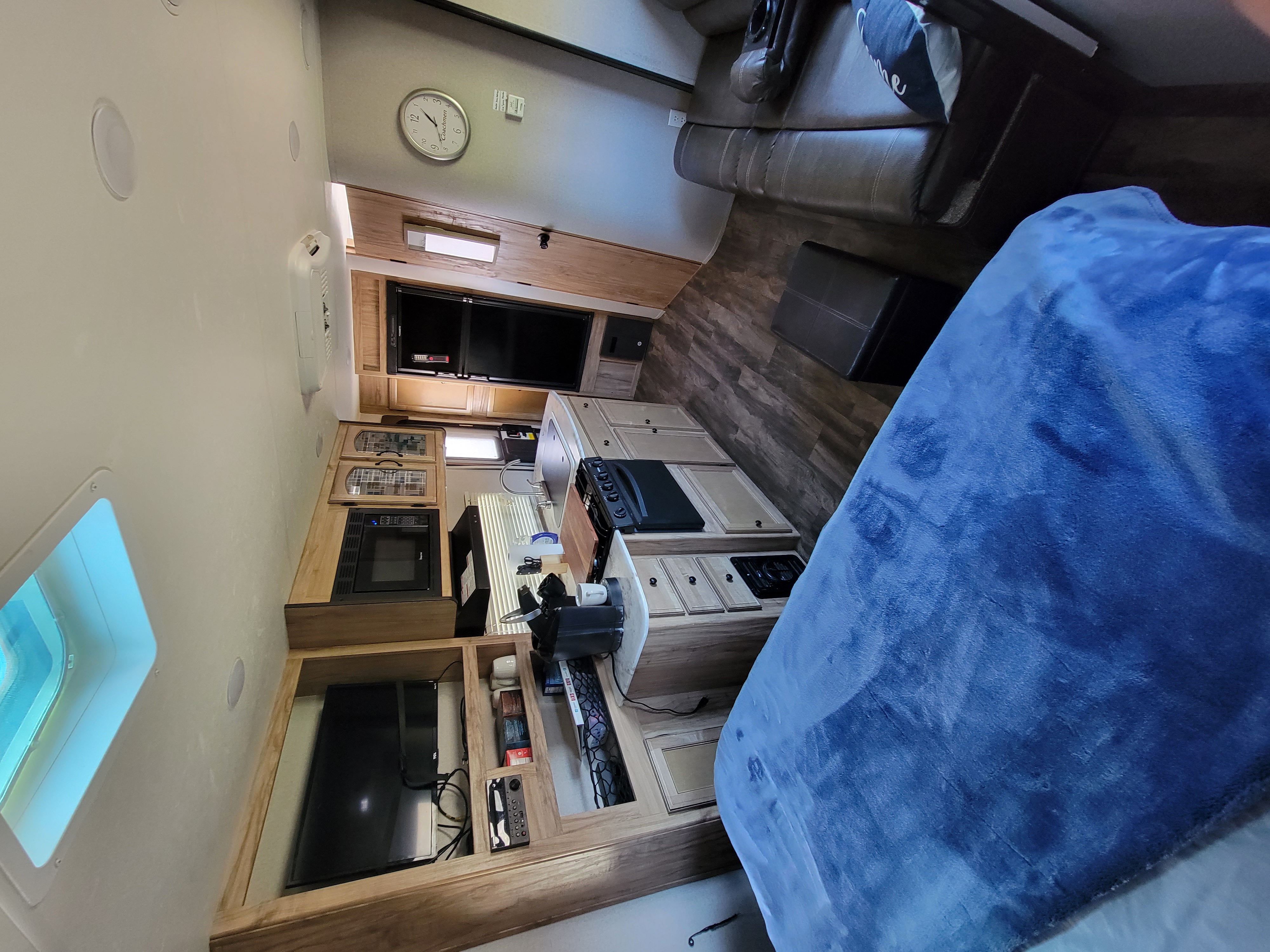 RV rental interior: A cozy living area with a couch and TV, plus a functional kitchenette. A blue blanket covers the sleeping space.. Coachmen 192 RBS 2018