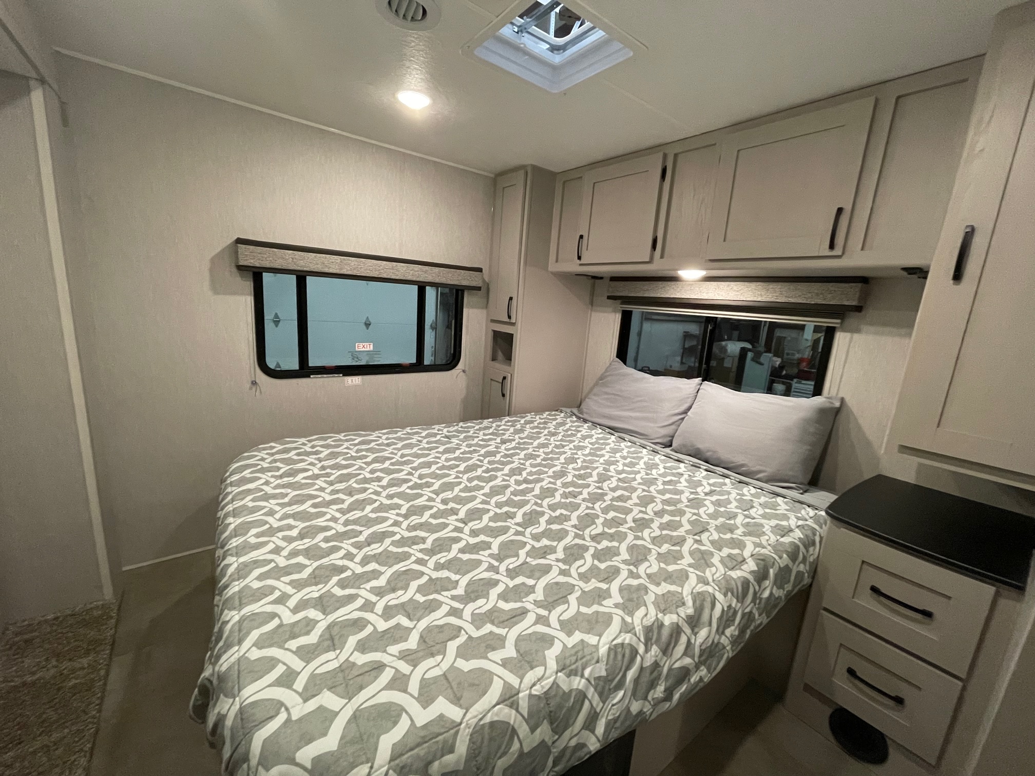 RV rental bedroom featuring a bed with a gray patterned comforter, light cabinetry, and large windows providing a view outside.. Coachmen Freelander 2024
