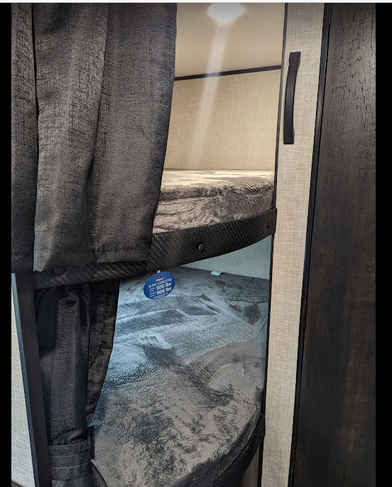 Inside an RV rental: Bunk beds with dark privacy curtains and a visible weight capacity tag.. Jayco 261BHS 2024