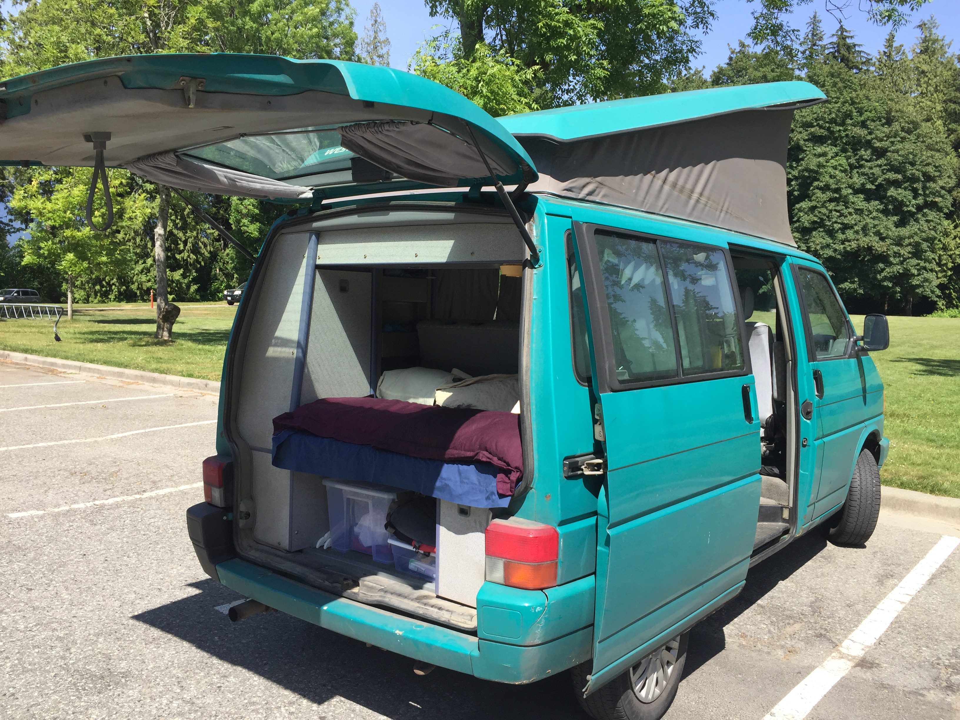 A teal camper van with an extended pop-top and open rear, revealing a bed & storage. Perfect for an rv rental trip.. Volkswagen T4 Westfalia Coach 1992