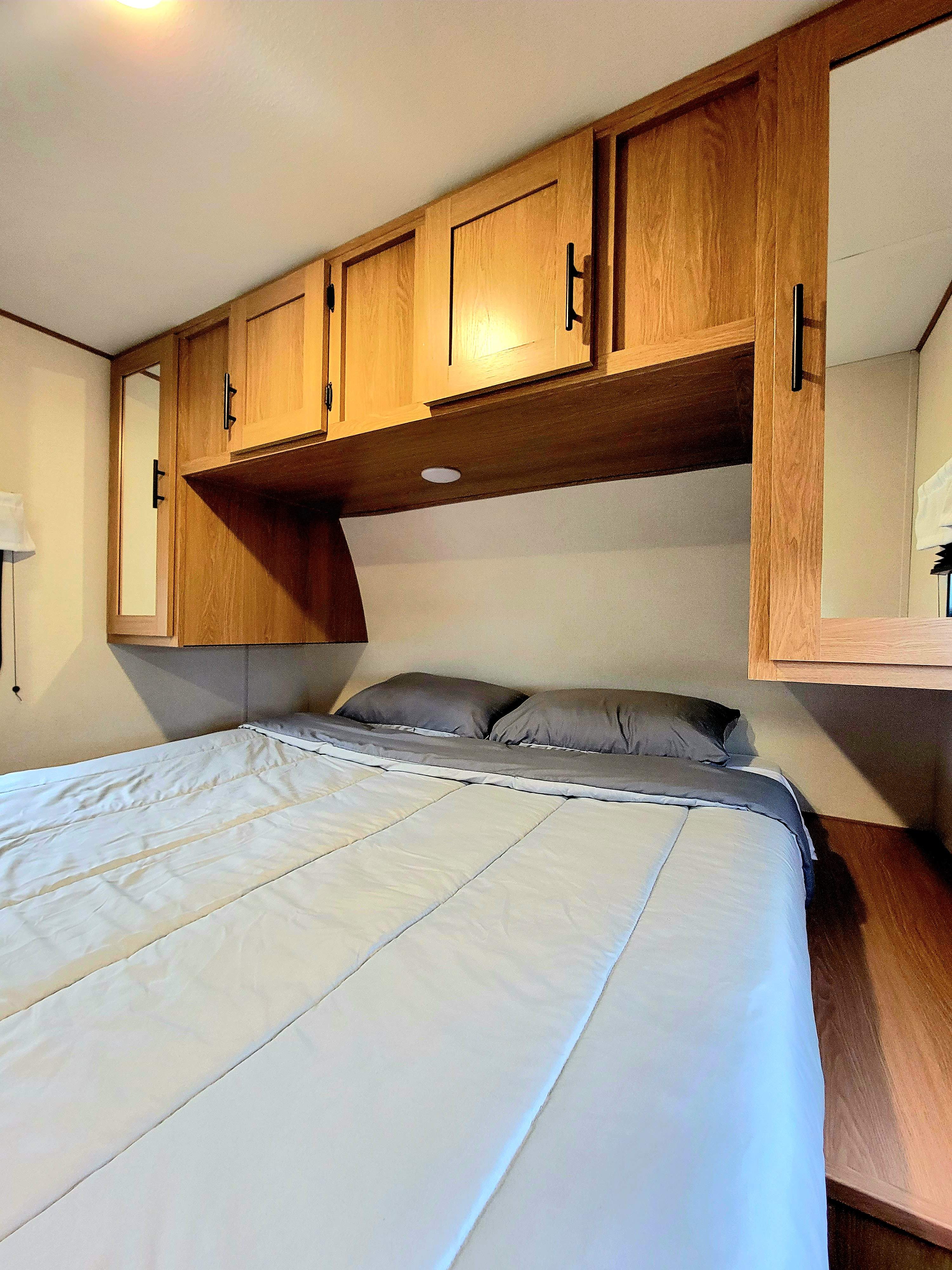 Cozy RV rental bedroom featuring a comfortable bed, wood overhead cabinets, and built-in mirrors, ideal for travel.. Avenger Avenger Trailer 2022