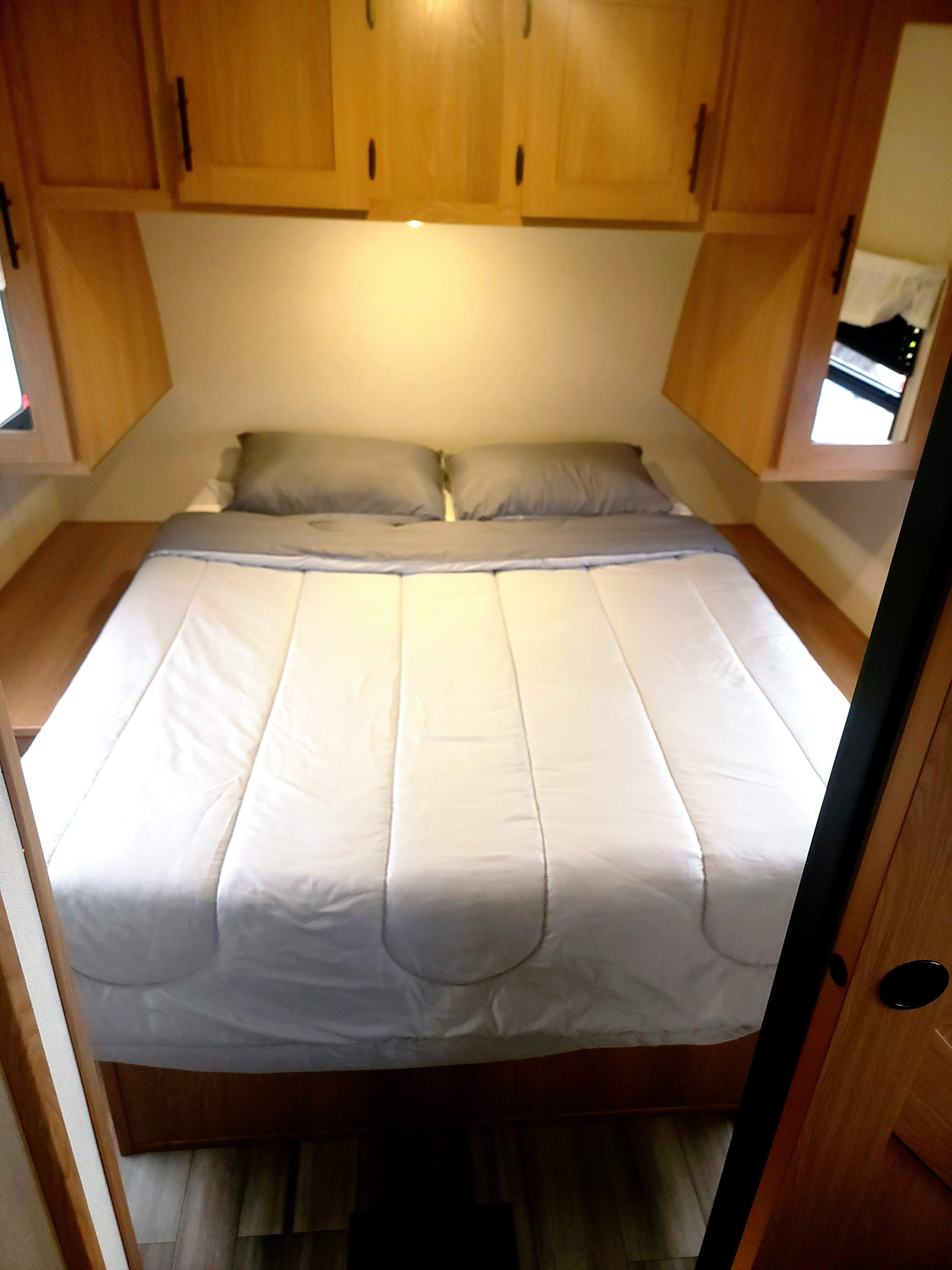 Compact RV rental bedroom with a cozy bed, overhead cabinets, and mirrored storage. Perfect for comfortable rest on your travels.. Avenger Avenger Trailer 2022