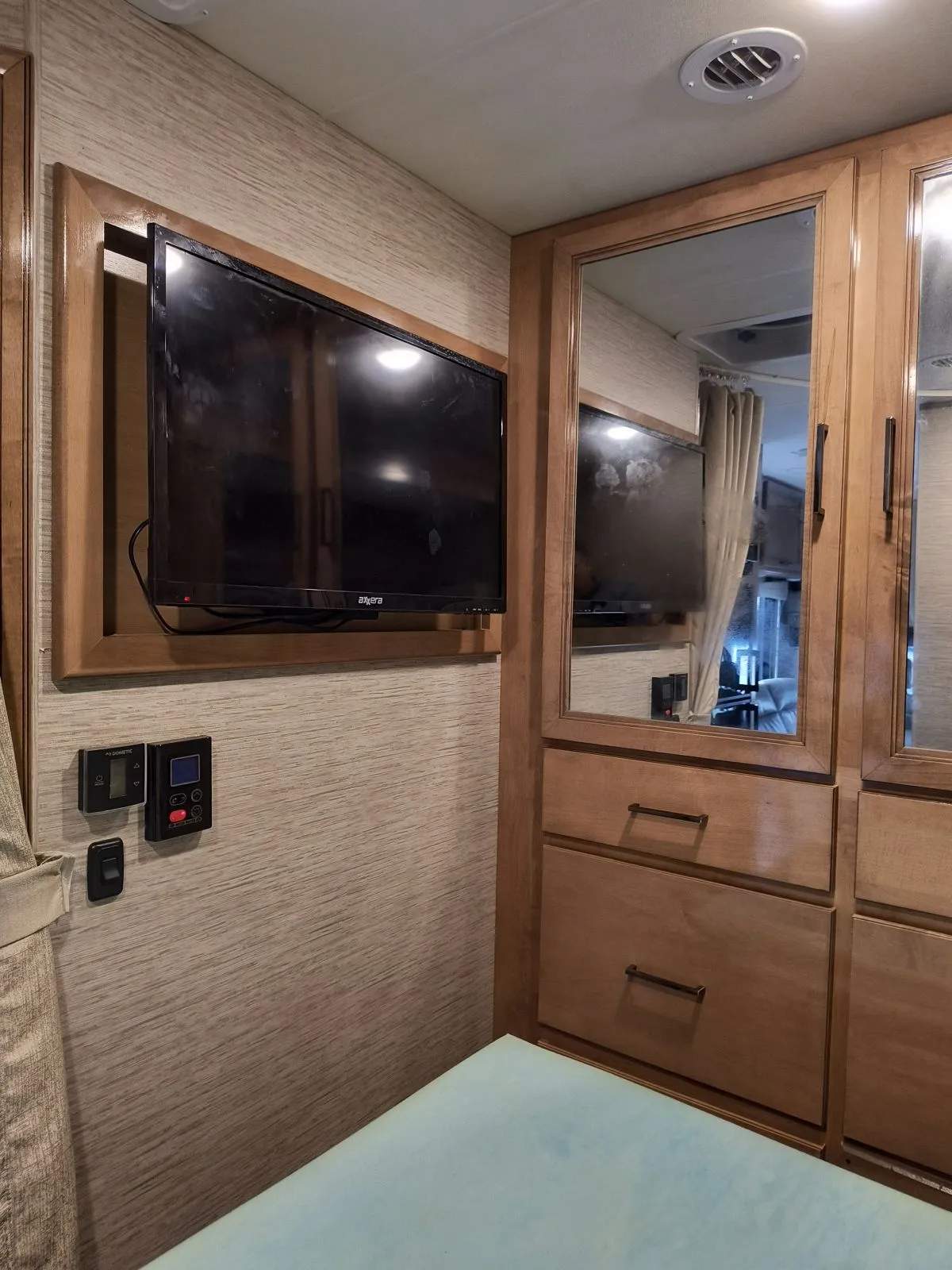 Inside an rv rental: a wall-mounted TV, Dometic controls, and mirrored cabinets with storage drawers beside the bed.. Thor Quantum 2021