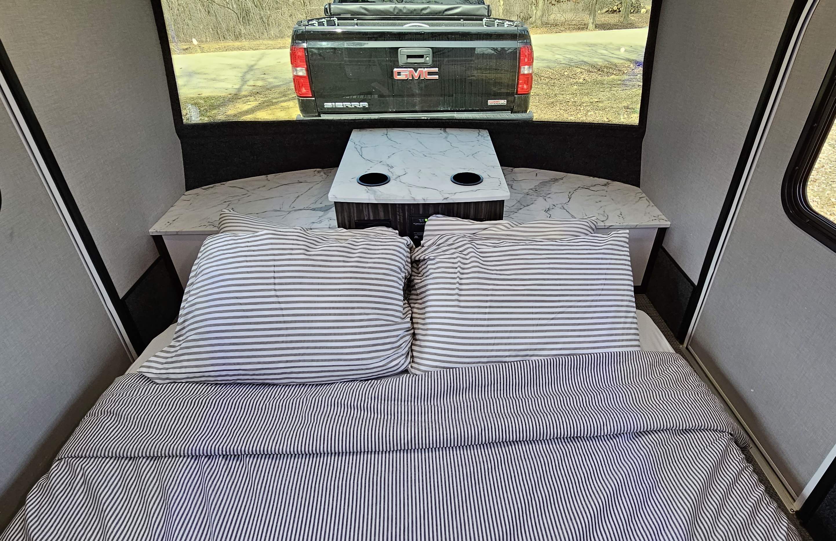 Cozy RV rental interior with striped bed, small table, and a view of a truck through the rear window.. InTech RV InTech RV Trailer 2020
