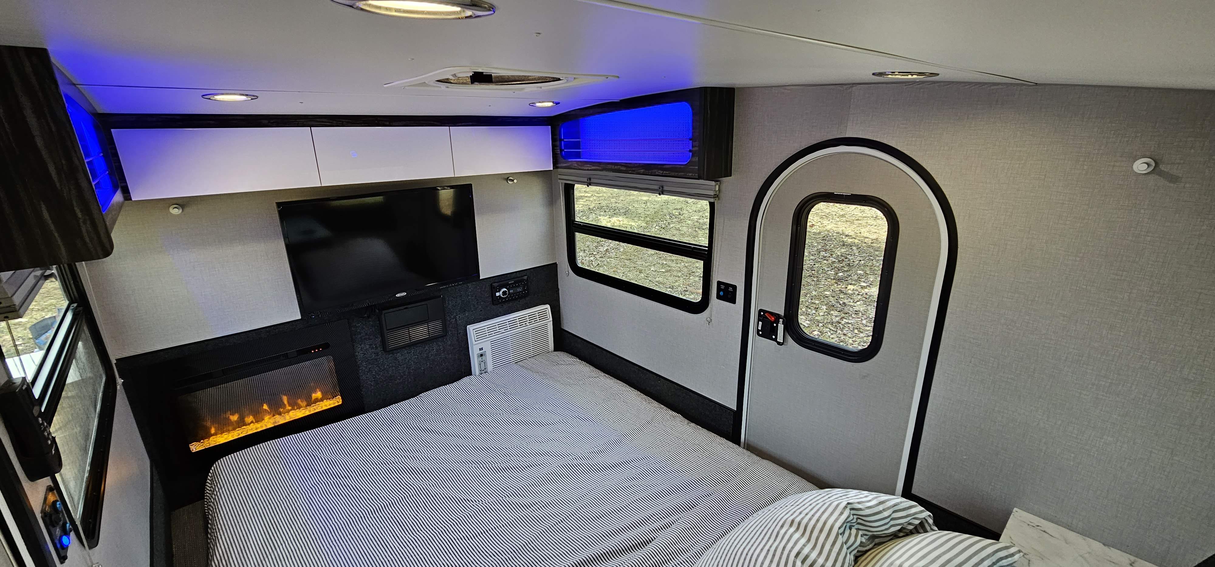 Step inside this cozy RV rental bedroom, complete with a striped bed, TV, electric fireplace, AC, and blue accent lighting.. InTech RV InTech RV Trailer 2020