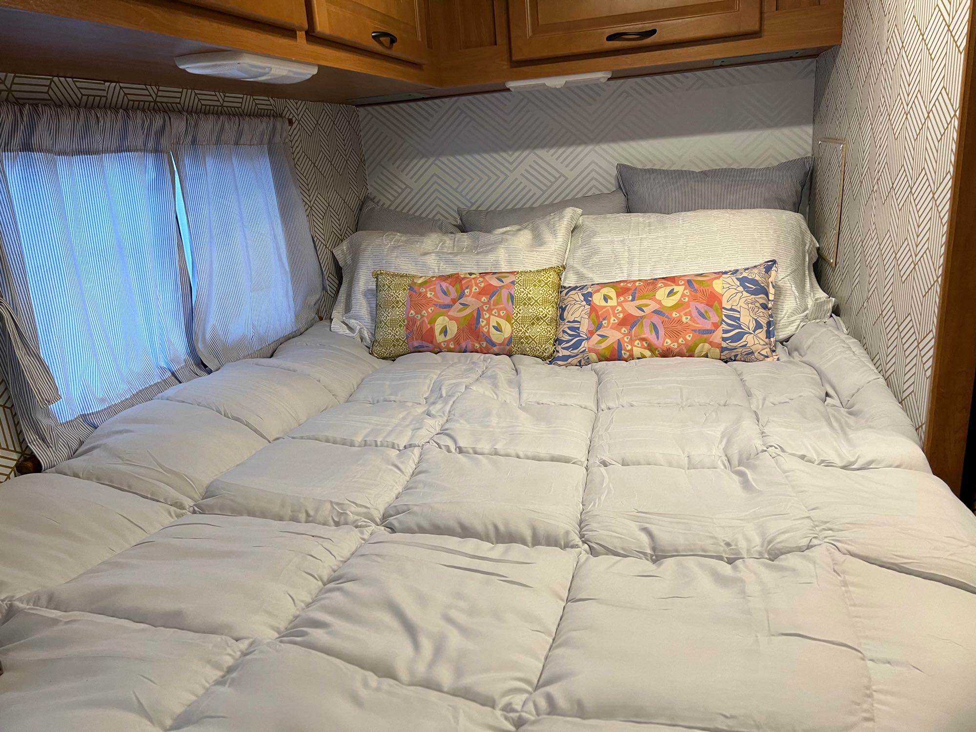 Explore this cozy RV rental bedroom featuring a comfy bed, modern patterned wallpaper, and practical wooden cabinets.. Thor Majestic 2016