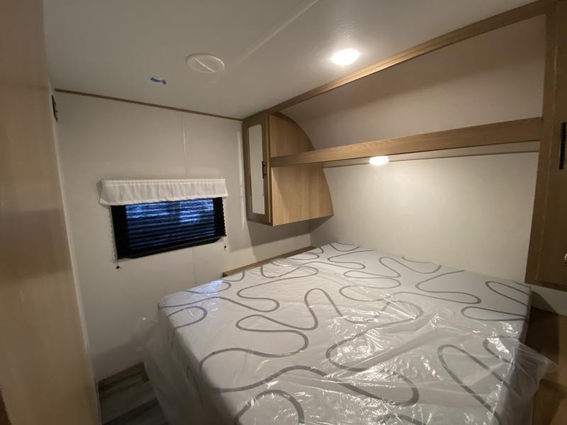 RV rental bedroom: bright interior with a plastic-covered mattress, overhead wood shelving, and a window for your journey.. Avenger LE 2022