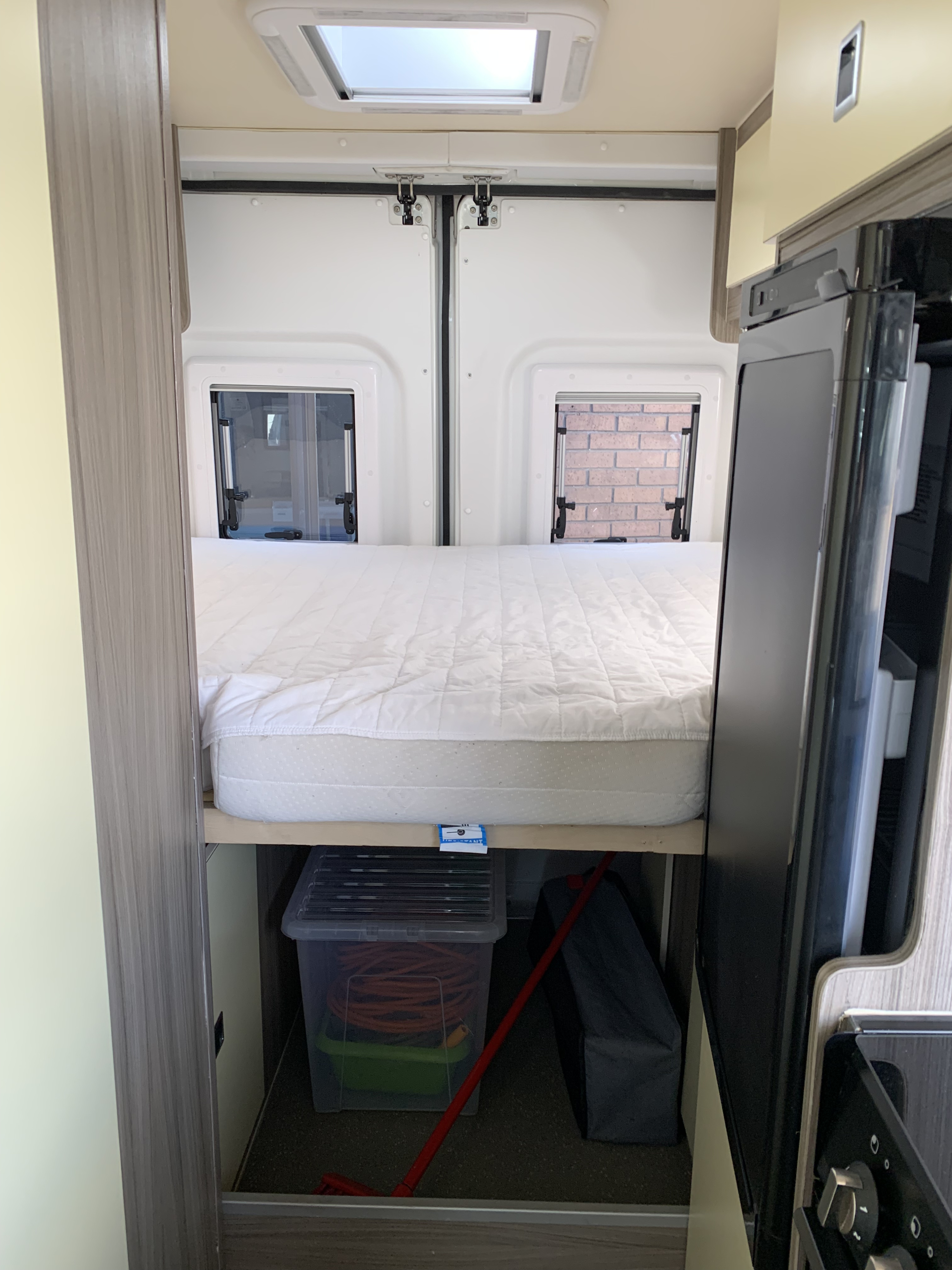 Spacious RV rental interior featuring a comfortable bed, overhead skylight, and under-bed storage, next to a compact kitchen area.. Peugeot Boxer 2021