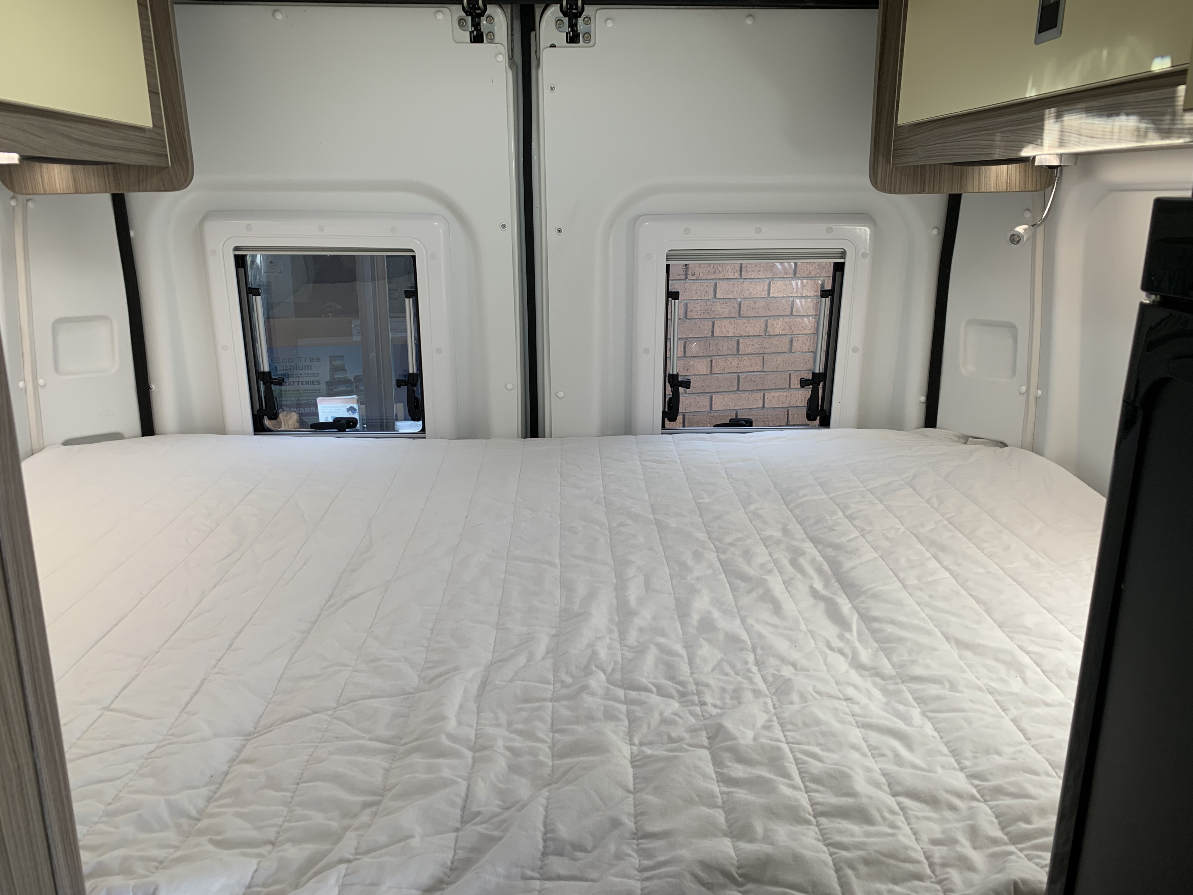 Cozy RV rental interior featuring a clean white bed, two rear windows, and overhead storage cabinets for comfortable travel.. Peugeot Boxer 2021