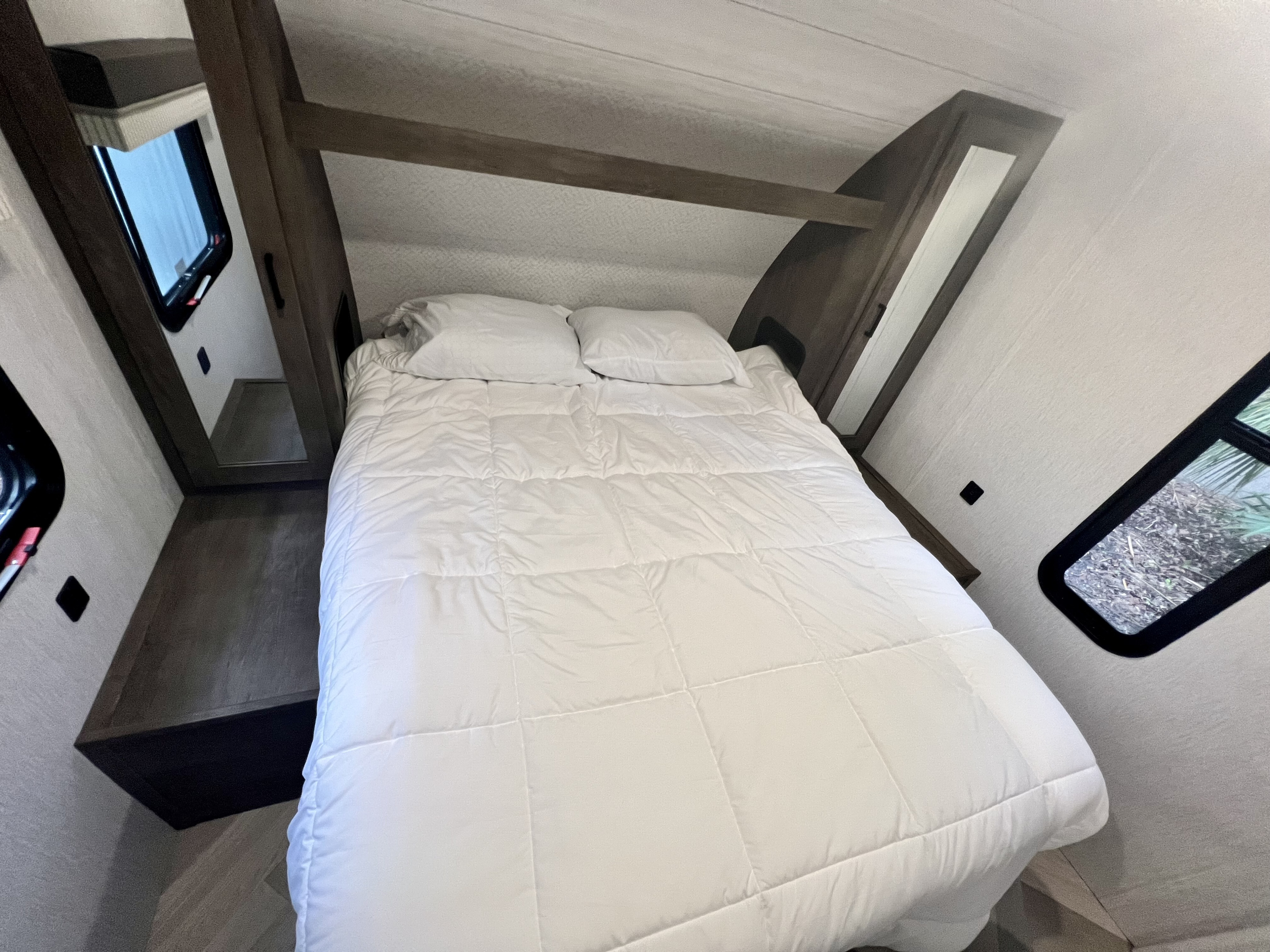 Inside an RV rental: a cozy bedroom with a white bed, built-in shelving, and windows. Ideal for travel.. Forest River Wildwood X-Lite 2022