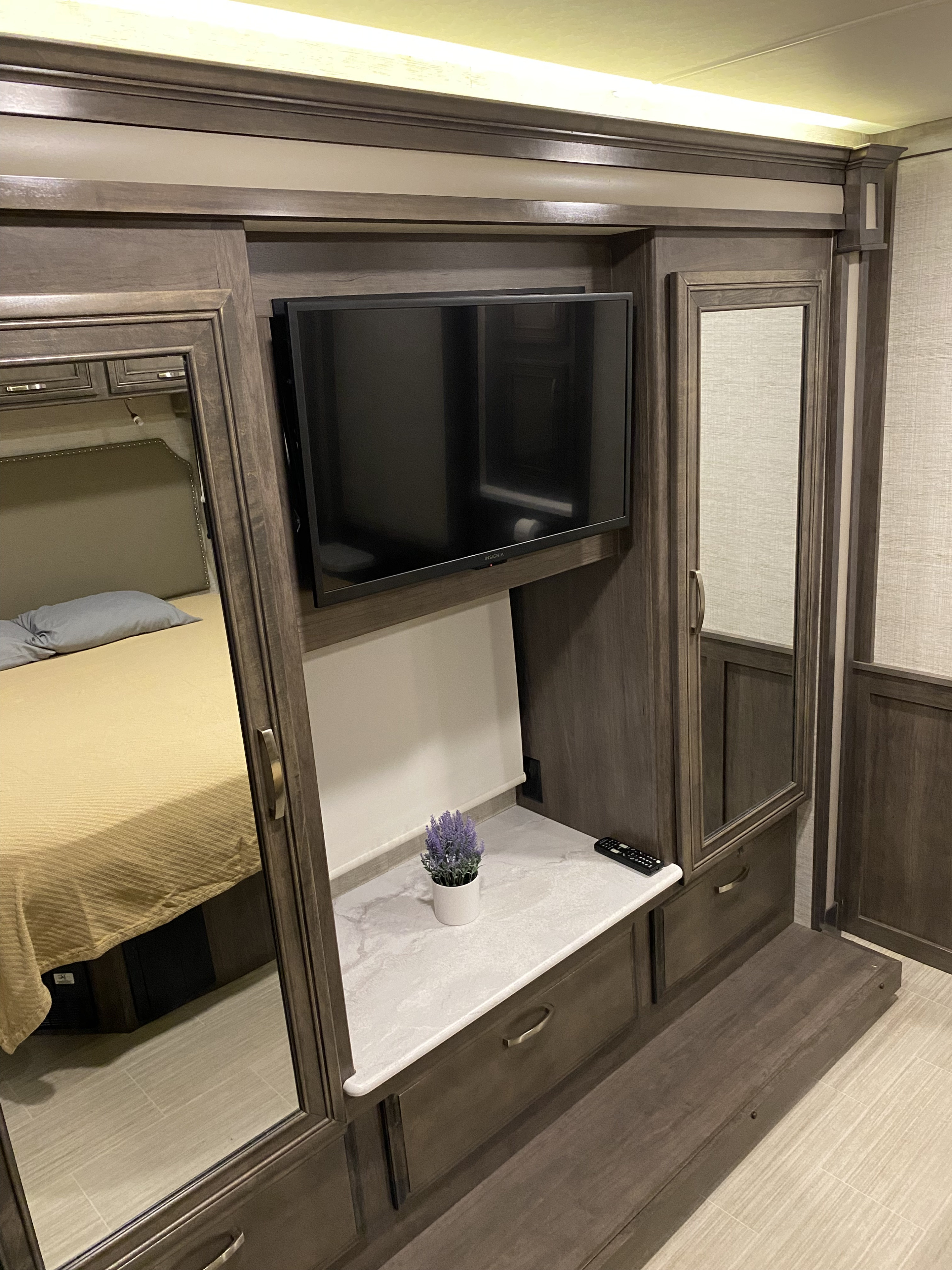 An RV rental bedroom features dark wood cabinetry, a mounted TV, and mirrored doors. The bed is visible in the reflection.. Jayco Precept 2021