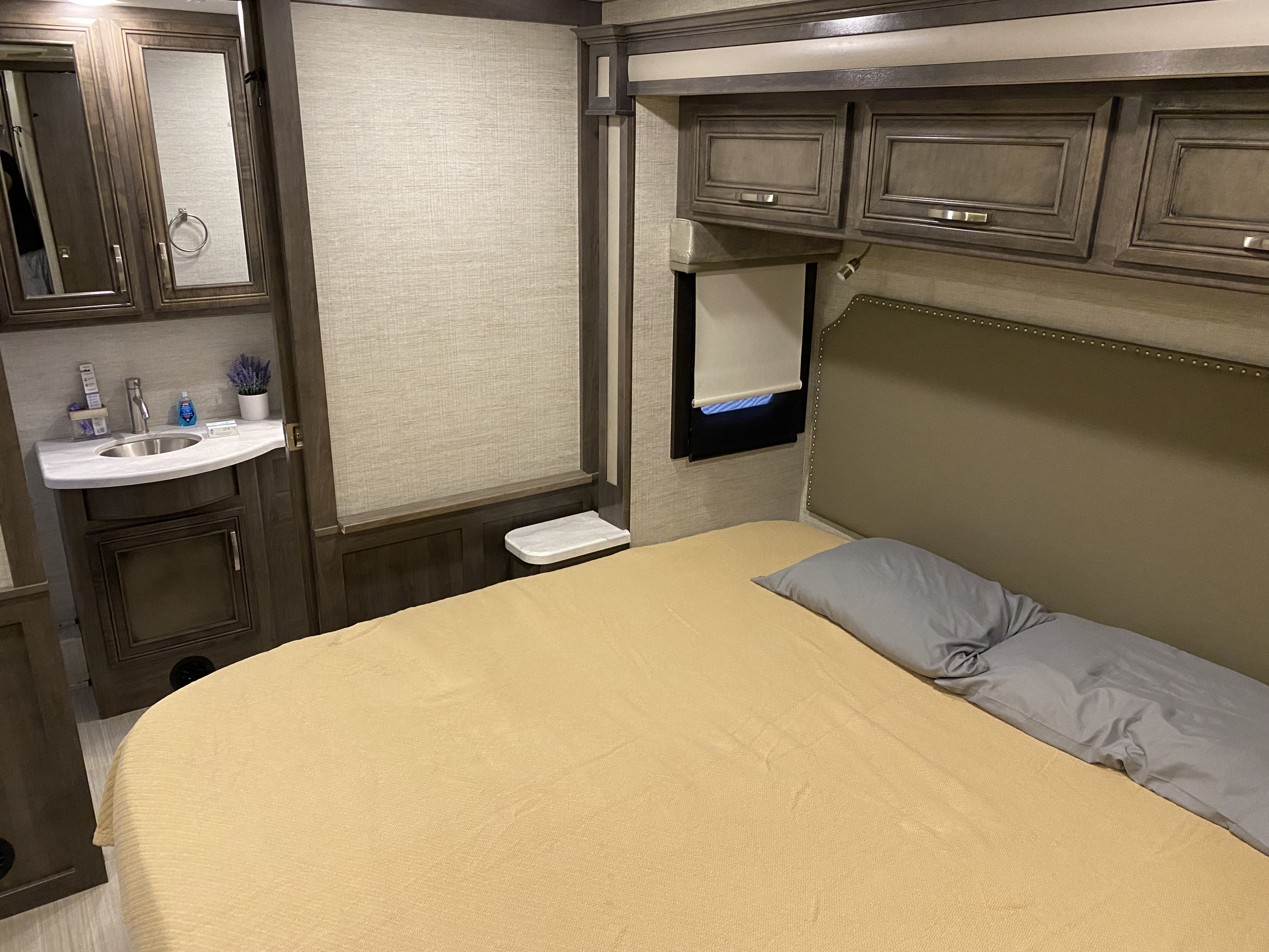 Cozy RV rental bedroom interior featuring a comfortable bed, compact vanity area, and overhead storage cabinets.. Jayco Precept 2021