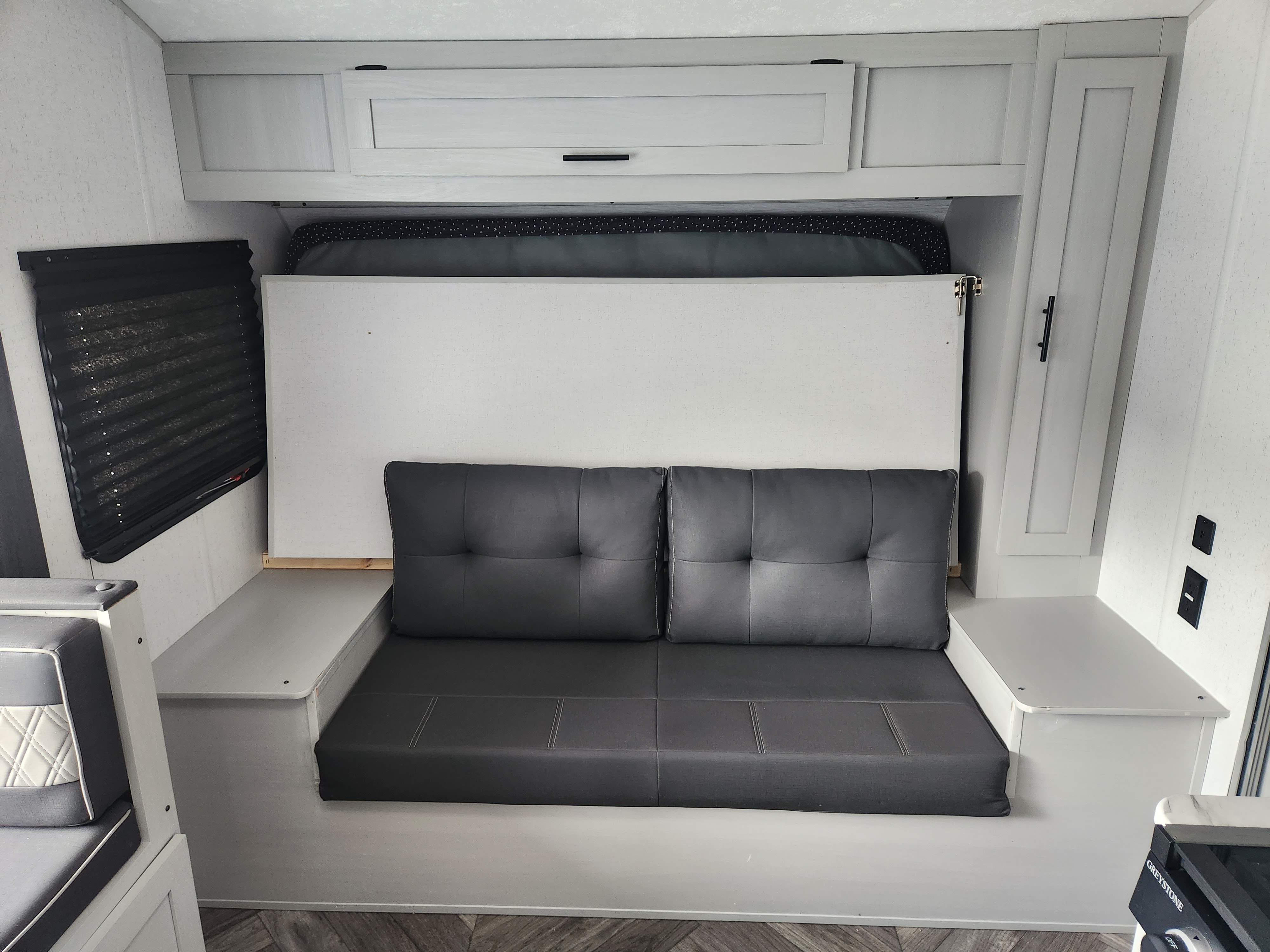 RV rental living space: a comfortable grey sofa, a wall-mounted bed above it, overhead cabinets, and window blind.. Forest River Salem FSX 2022
