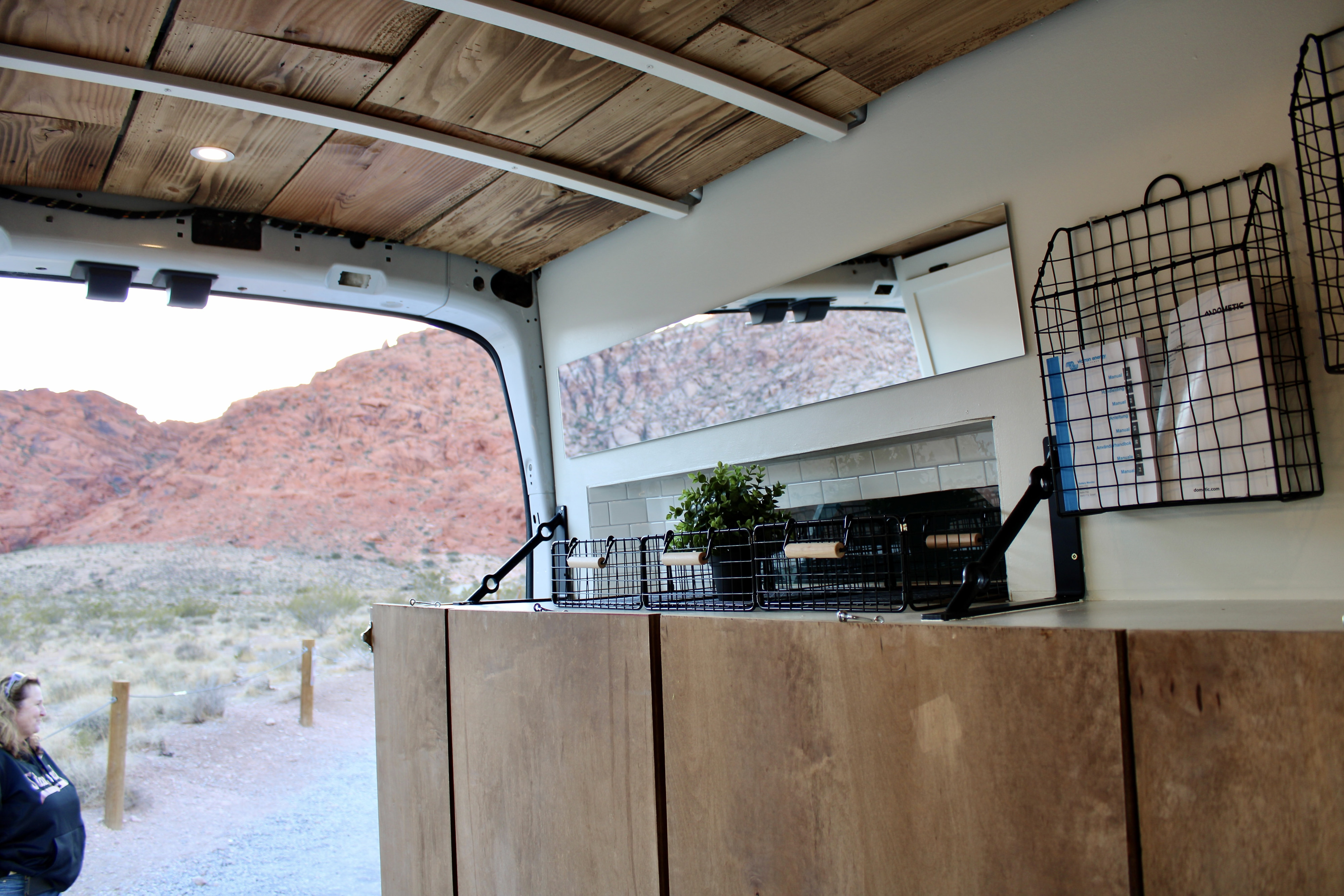 Inside a custom RV rental, a wood ceiling, integrated storage, and kitchen area provide comfort with a stunning desert view outside.. Ford Transit 2019