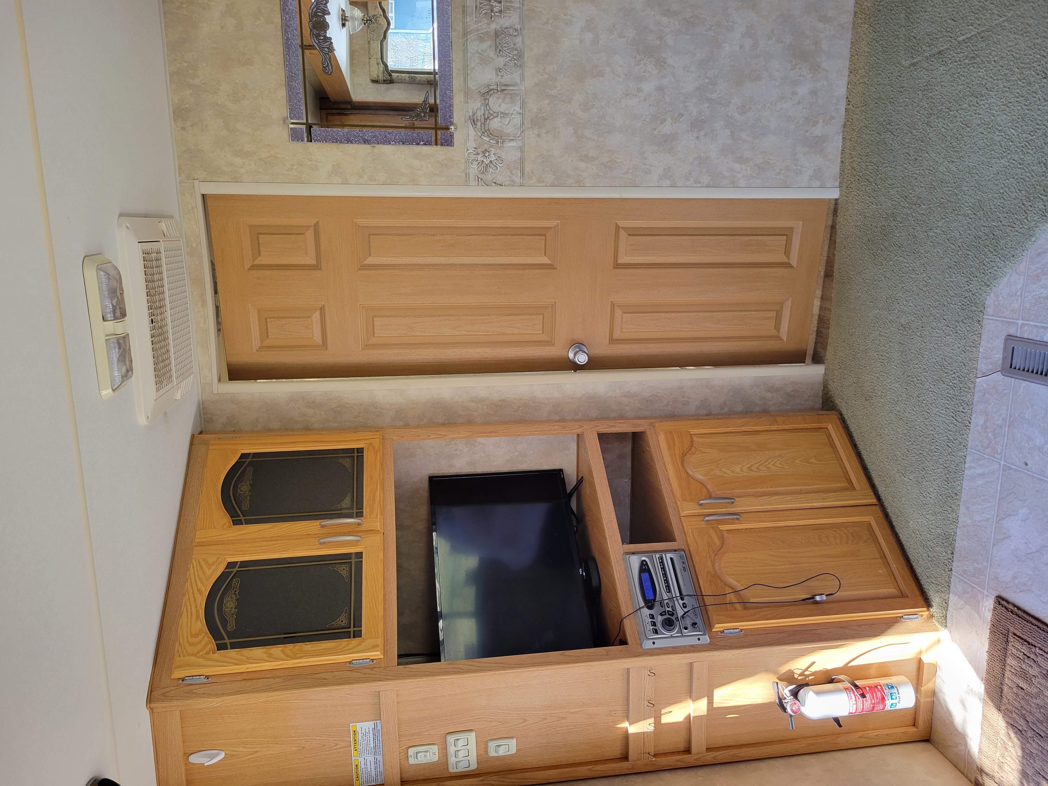 View inside an RV rental, showing a cozy entertainment center with TV, storage, and a safety fire extinguisher.. Prowler Prowler Trailer 2007