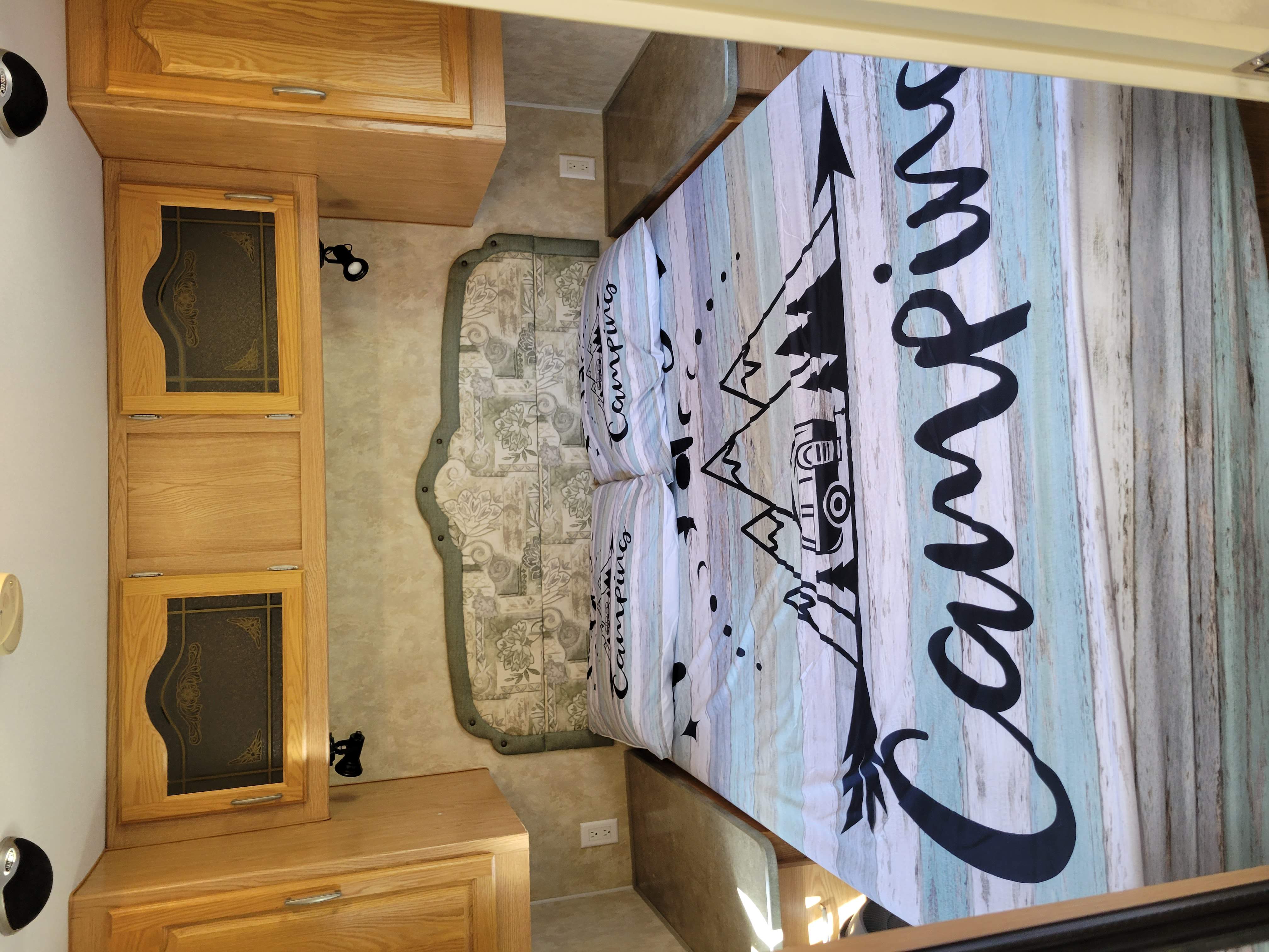 RV rental bedroom view: features a 'Camping' themed bed, oak cabinets, and compact storage for travel.. Prowler Prowler Trailer 2007