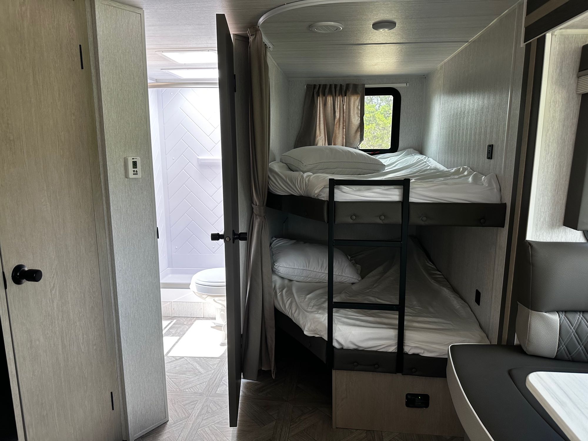 Experience RV rental comfort: twin bunk beds, a compact bathroom, and a dinette in a modern camper.. Forest River Wildwood X-Lite 2023