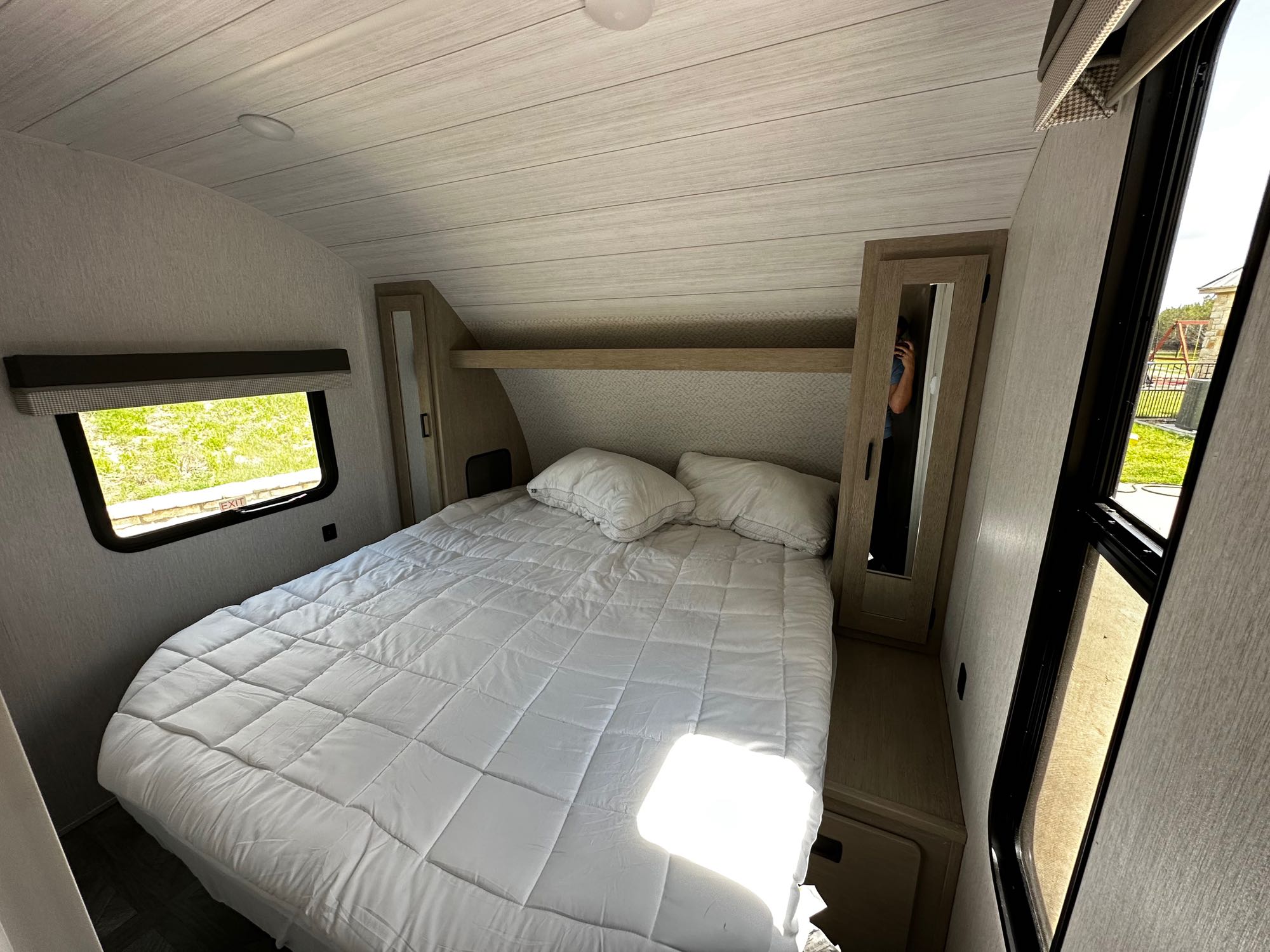 Clean and spacious RV rental bedroom featuring a large white bed, built-in storage with mirrors, and bright windows.. Forest River Wildwood X-Lite 2023