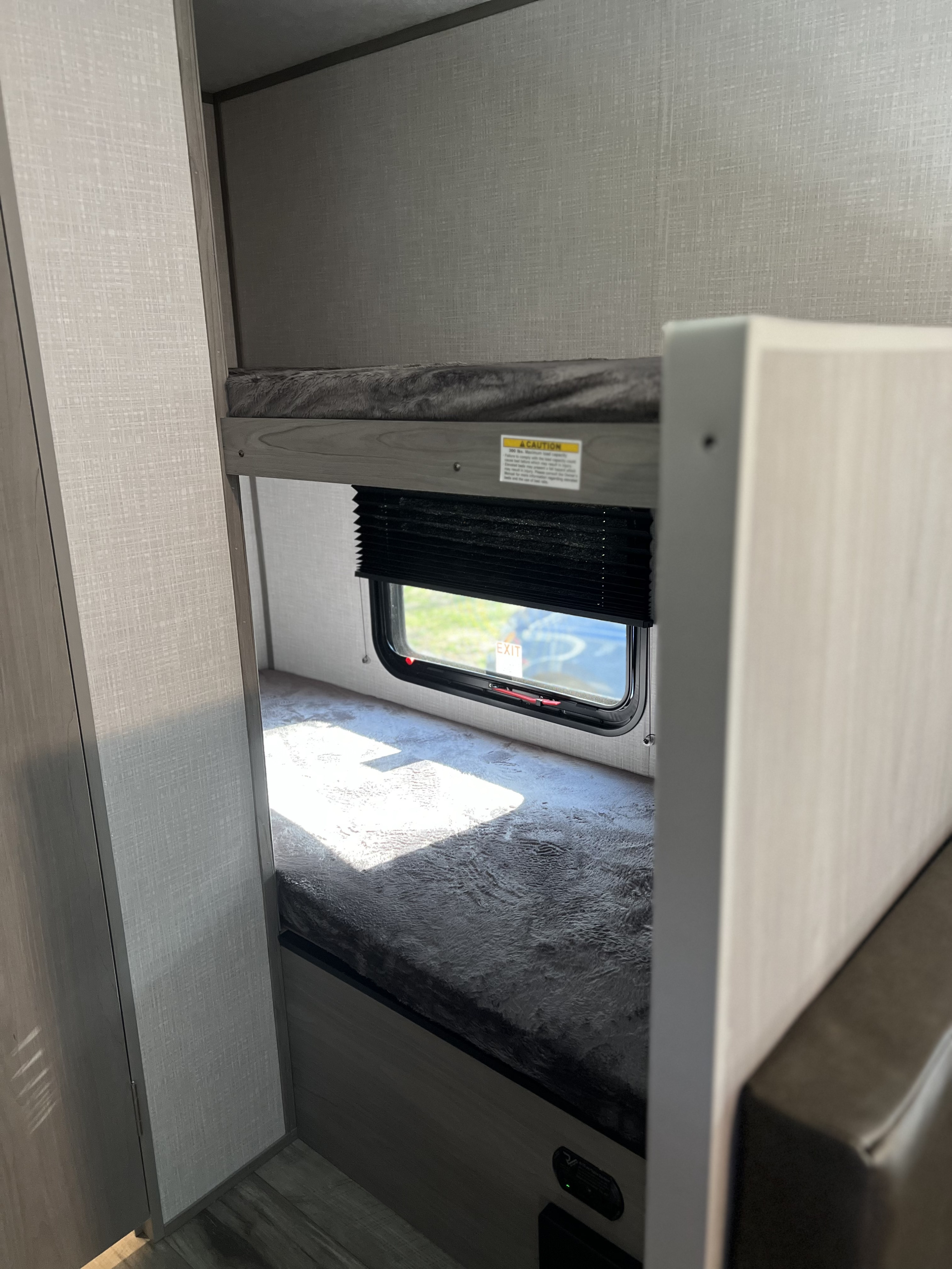 Inside an RV rental, a compact sleeping area features stacked bunk beds, with sunlight shining through a window.. Dutchmen Coleman Lantern LT 2023