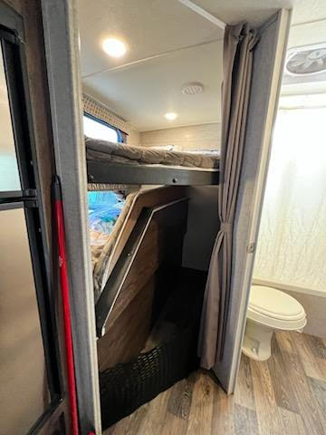 Inside an RV rental: a cozy bunk bed area is visible left, with a compact bathroom and toilet seen through the drawn curtain on the right.. Forest River Rockwood Mini Lite 2018