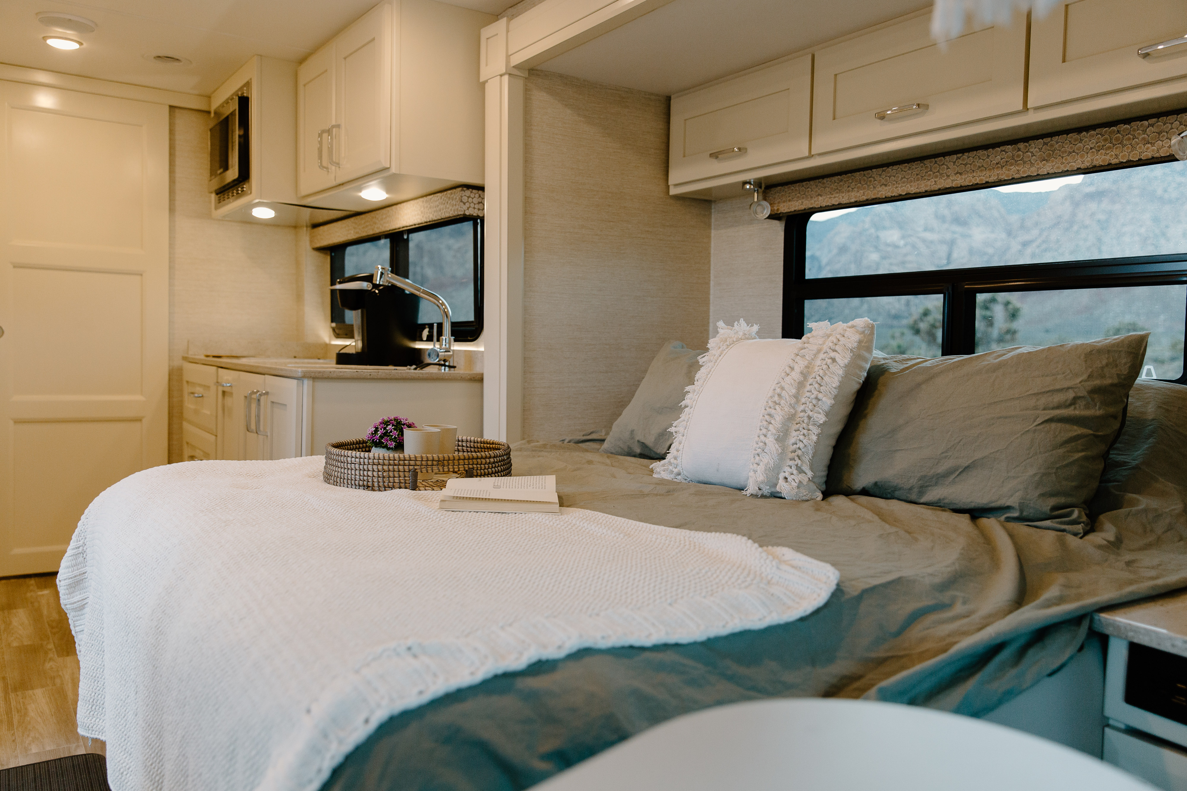 Cozy RV rental interior: bed with reading nook and tray, compact kitchen, and scenic mountain views for comfy travel.. Tiffin Motorhomes Wayfarer 25 JW 2021