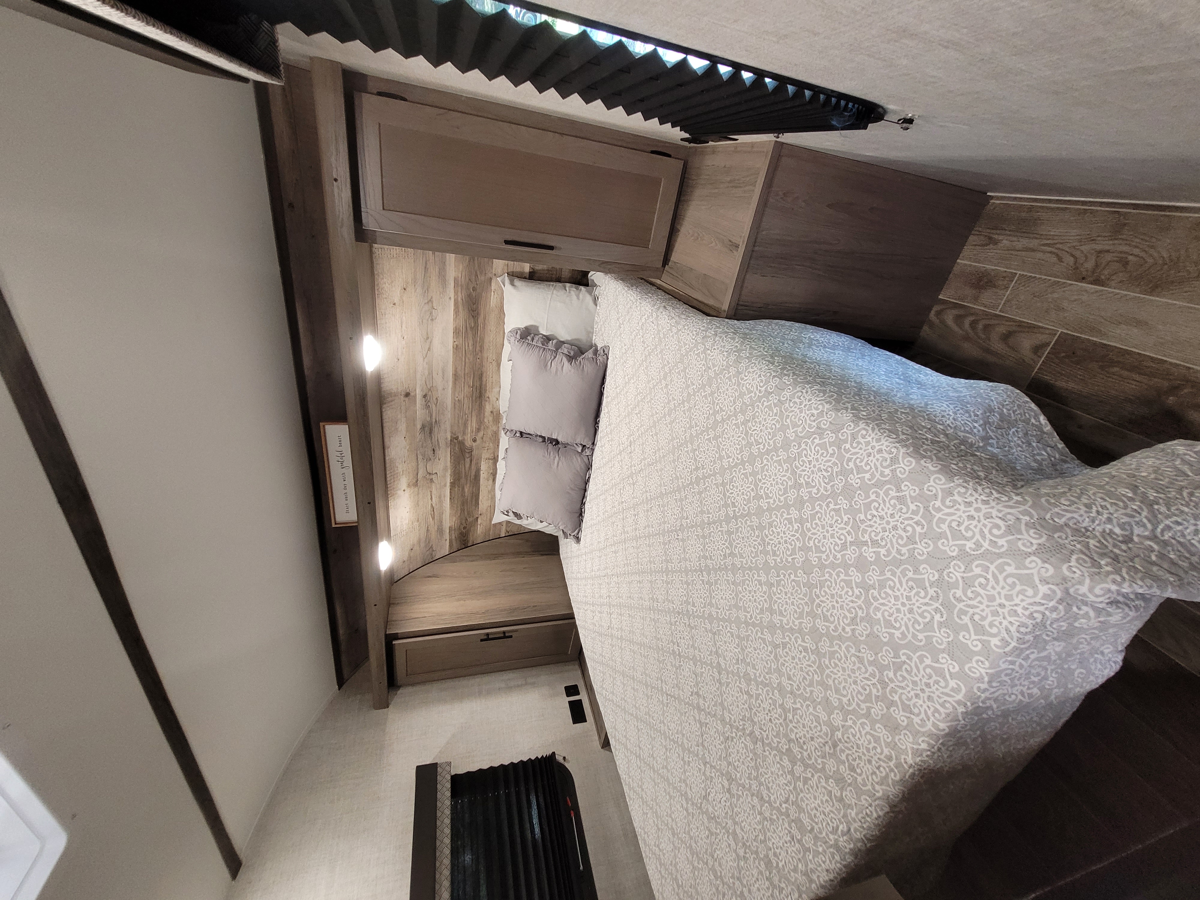 Cozy RV rental bedroom features a comfortable bed with patterned comforter, wood walls, and overhead storage.. Gulf Stream Friendship 2022