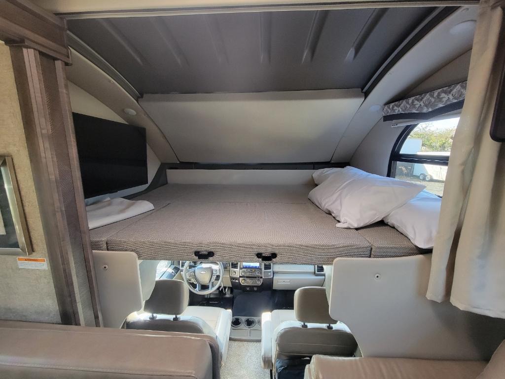 Spacious RV rental interior with a comfortable cab-over bed, white pillows, TV, and view of the cockpit.. Thor Motor Coach OMNI 36RS 2021