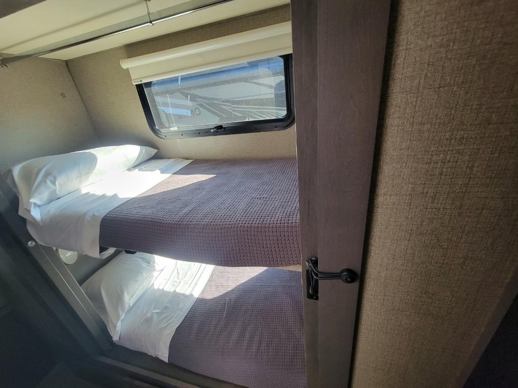 Inside an RV rental: two neatly made bunk beds with window above. A comfortable, compact sleeping area for your trip.. Thor Motor Coach OMNI 36RS 2021