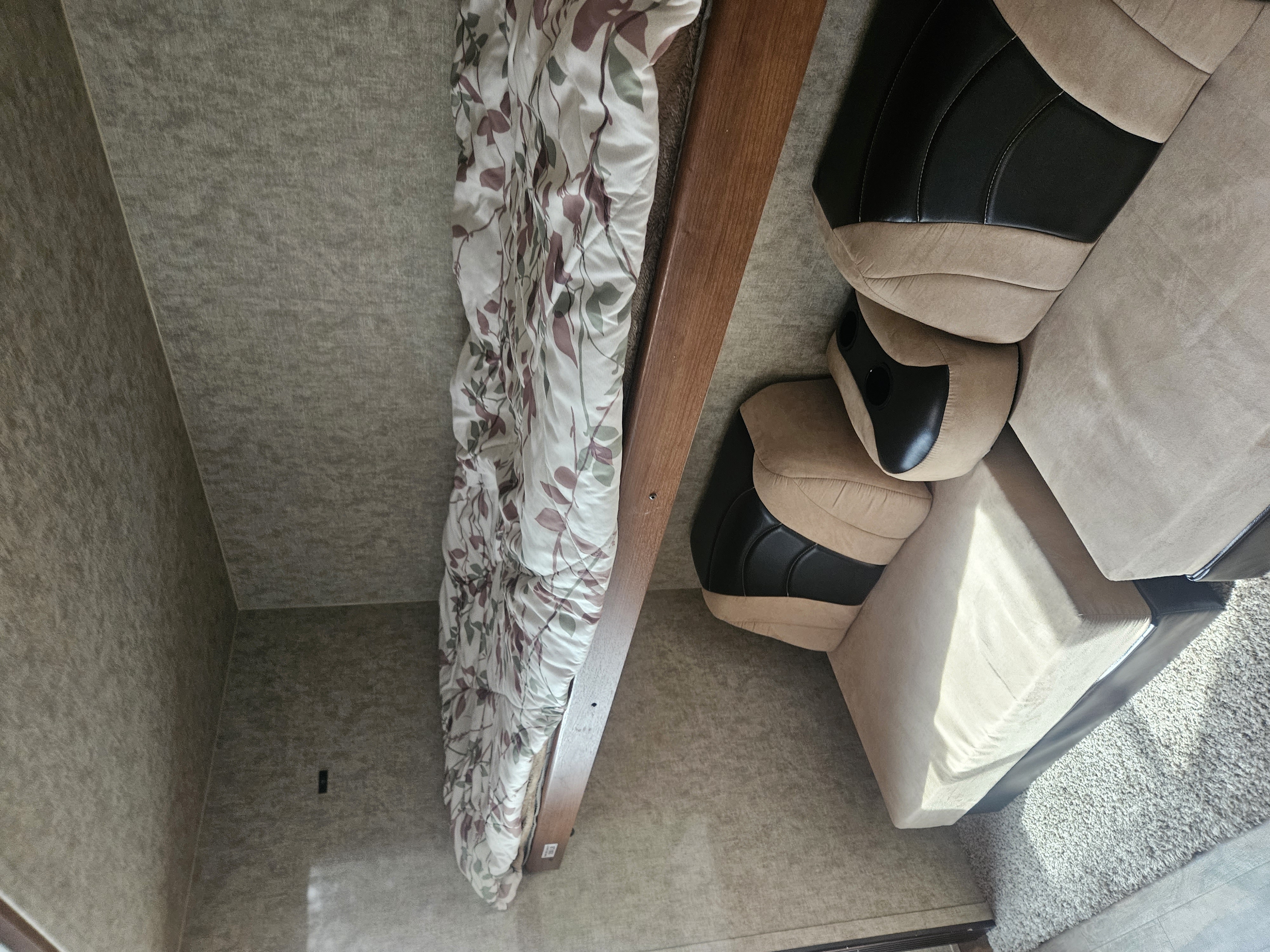 Cozy RV rental interior: floral bedding on wooden frame, textured walls/floor, and a two-tone beige/black sofa with light rug.. Prime Time Tracer 2018