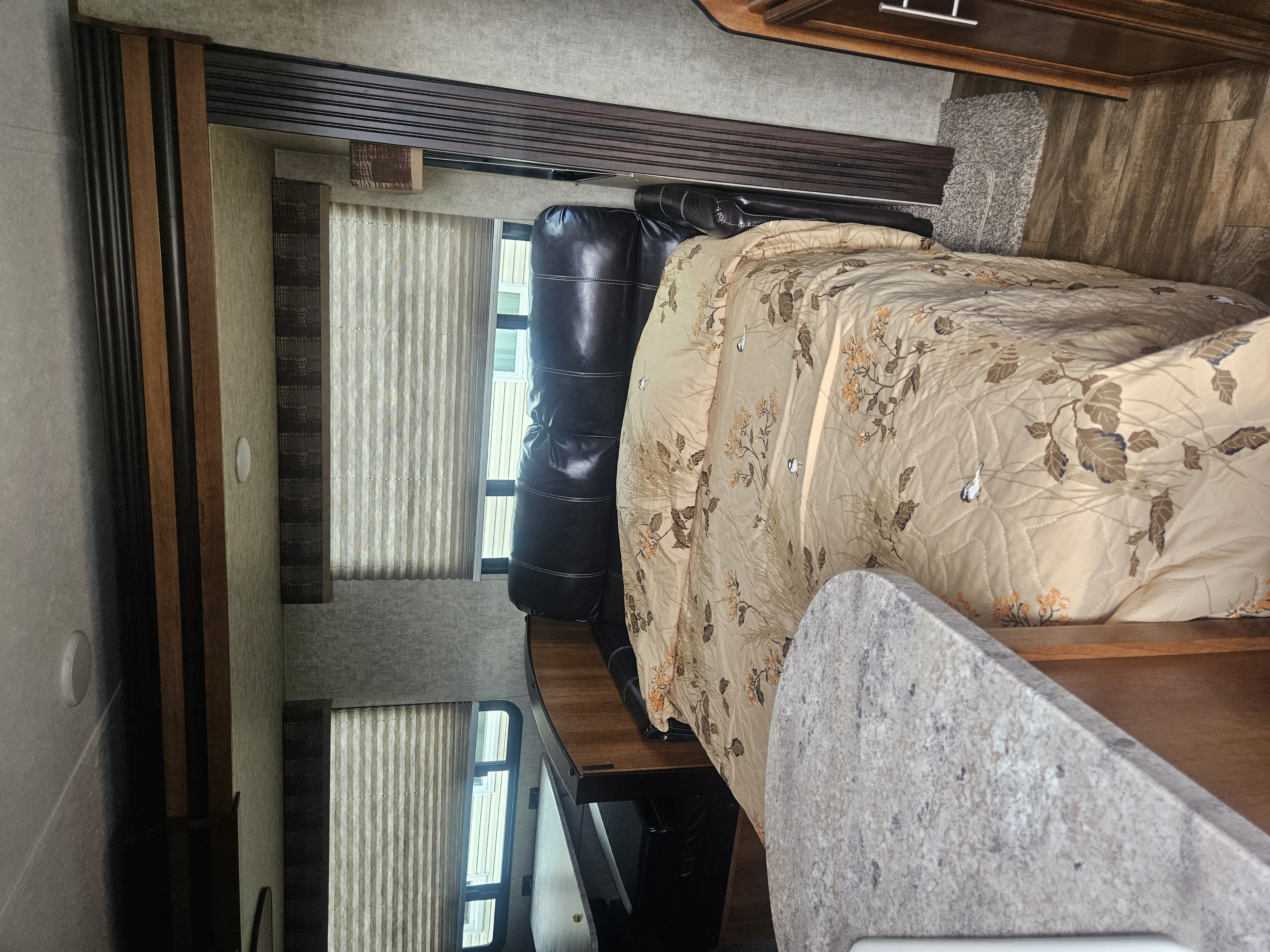 Cozy RV rental bedroom with patterned comforter, dark sofa, and window blinds. Experience comfortable travel.. Prime Time Tracer 2018