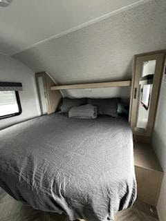This inviting RV rental bedroom features a queen bed with grey bedding, overhead storage, and a window for comfortable mobile living.. Forest River Evo 2023