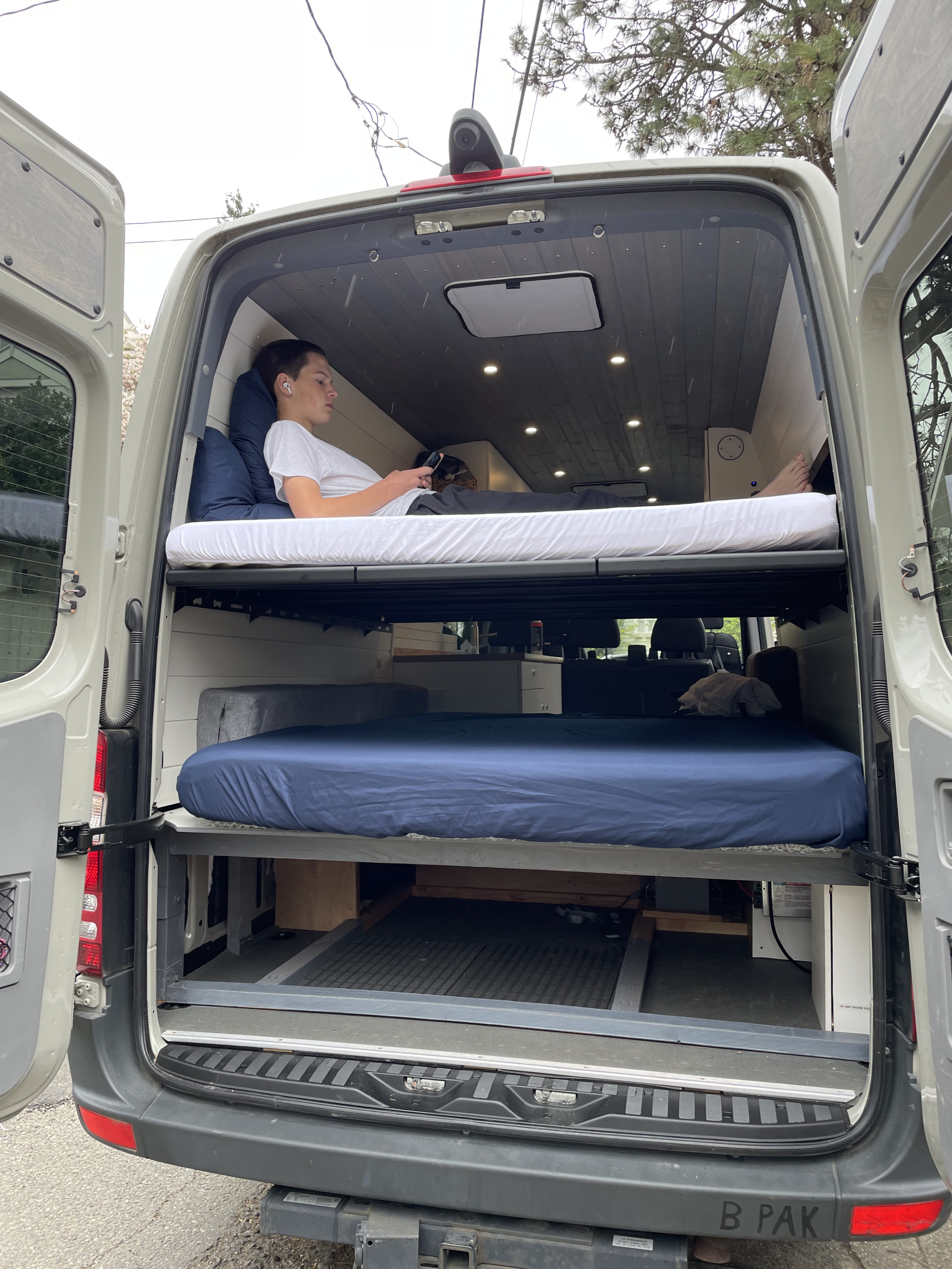 Inside an RV rental, this camper van features bunk beds for mobile living. A person relaxes on the top bunk, ideal for travel.. Mercedes-Benz Sprinter 2018