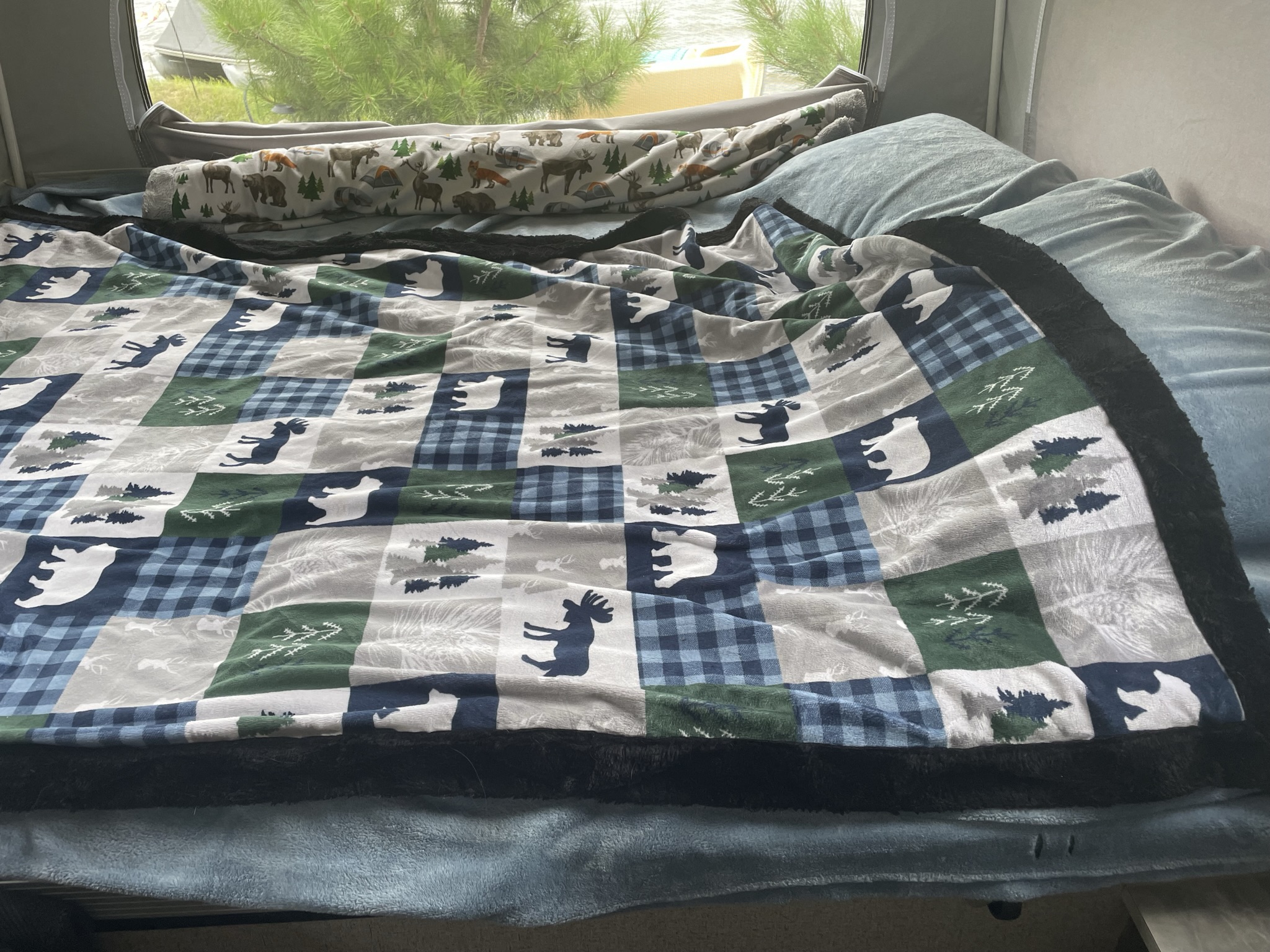 Cozy RV rental bed, featuring a wilderness blanket and rolled pillow, with scenic views outside.. Forest River Rockwood ESP 2020