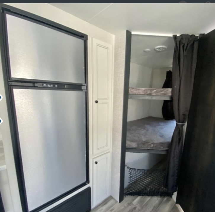 RV rental interior featuring a refrigerator, white storage cabinet, and bunk beds with dark privacy curtains and a storage net.. Highland Ridge RV Open Range Lite 2023