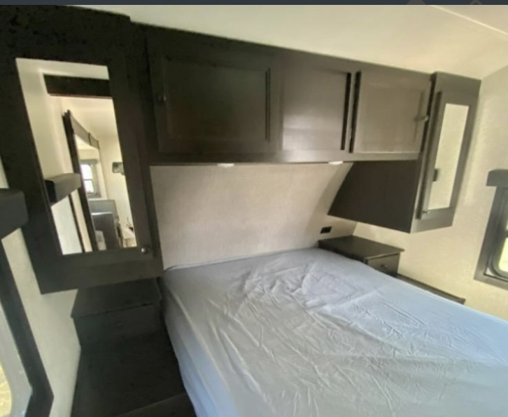 This cozy RV rental bedroom features a comfortable bed, dark overhead cabinets, and a mirrored wardrobe. Ready for your adventure!. Highland Ridge RV Open Range Lite 2023